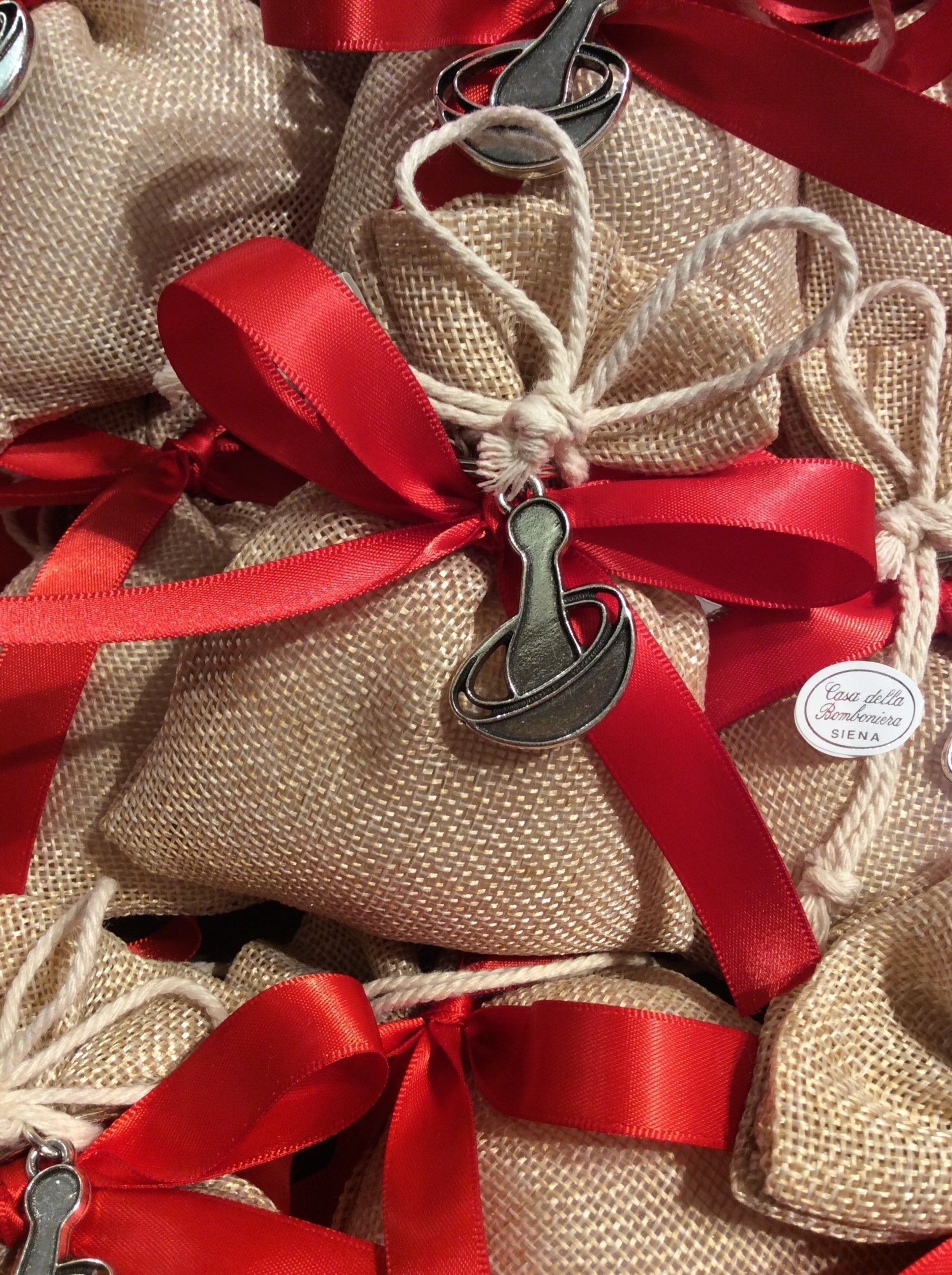 Sacchetti regalo avvolti con fiocchi di nastro rosso e spago, con un piccolo ciondolo pendente su tessuto di iuta beige.