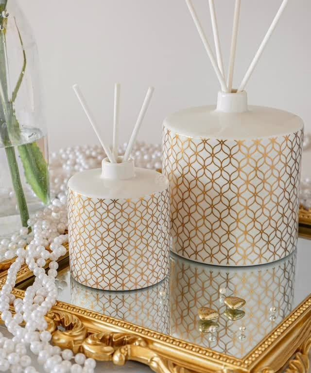 Due diffusori a bastoncini con decorazioni dorate su un vassoio a specchio con decorazioni in perle.