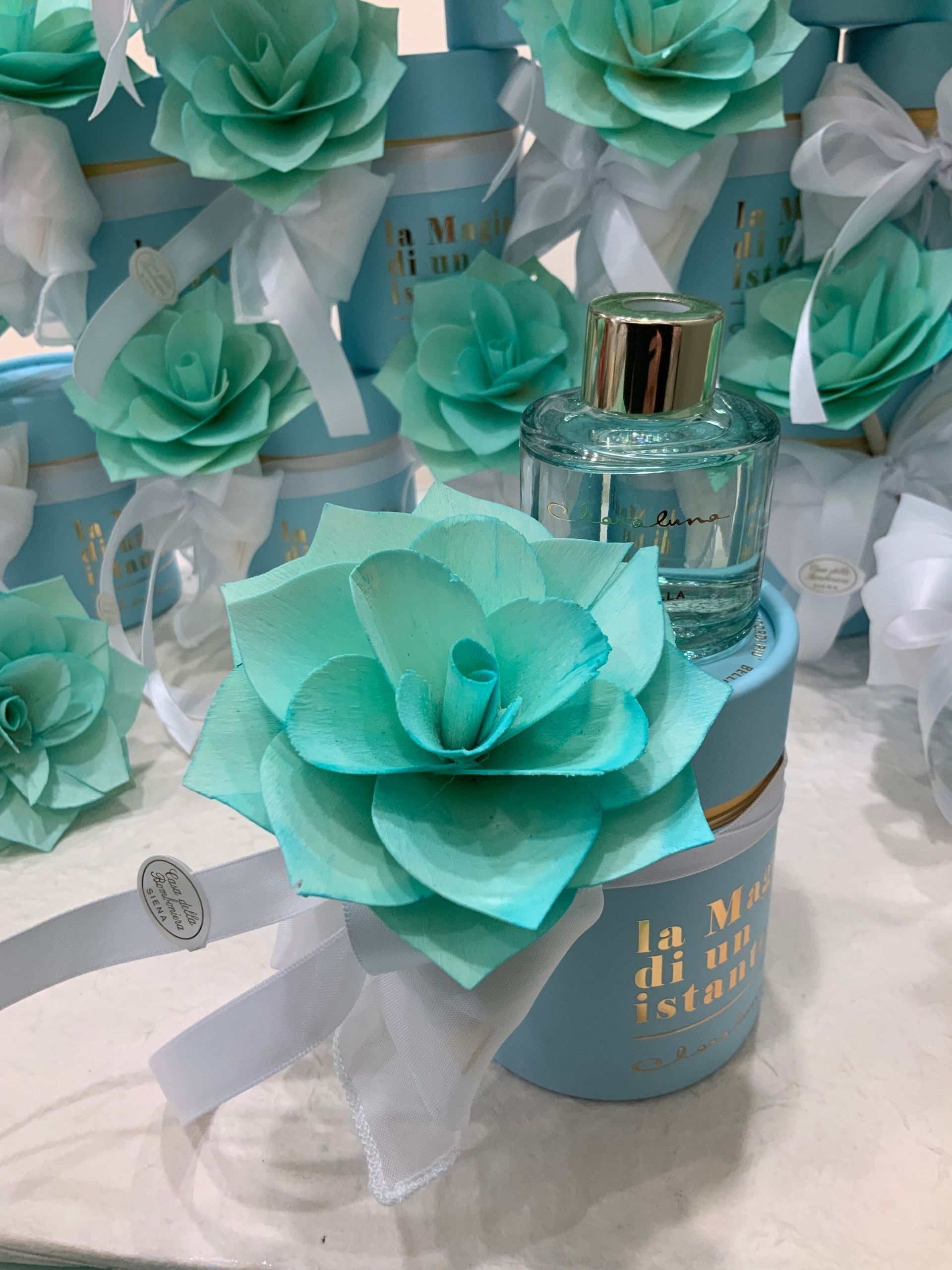 Fiori di carta color verde acqua e barattoli regalo scintillanti disposti su un tavolo bianco in una composizione decorativa.