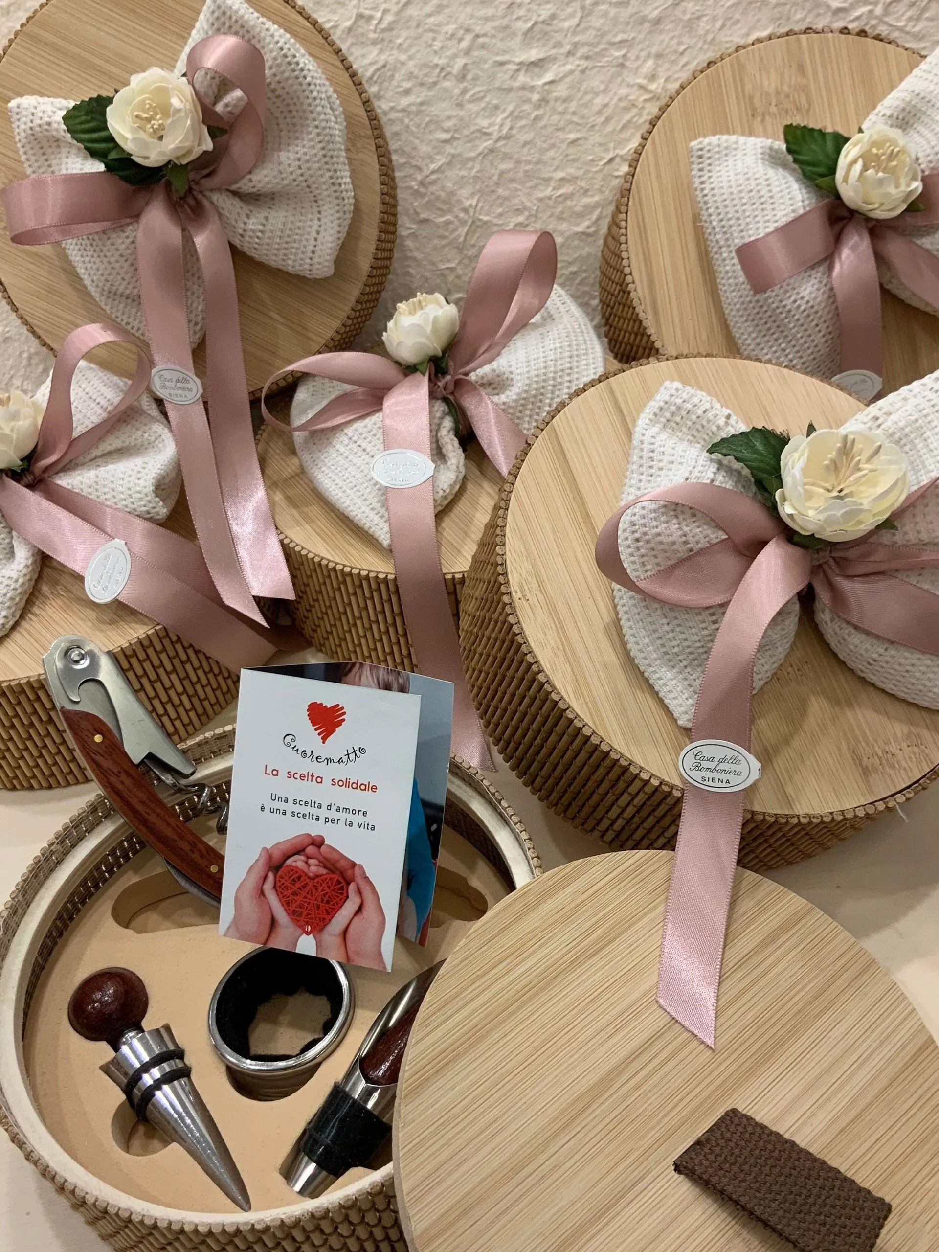 Bomboniere fatte a mano con fiori di nastro rosa su fette di legno rotonde, accompagnate da piccoli articoli per il trucco e accessori.