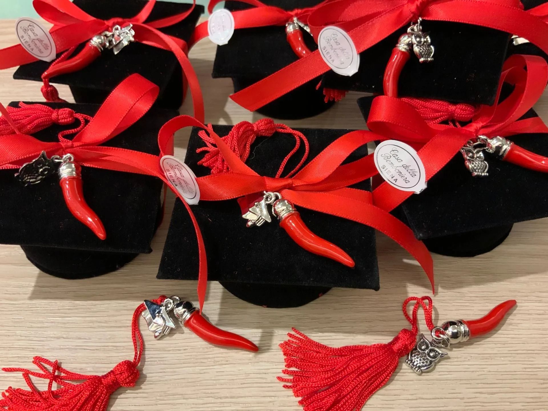 Ciondoli con nappe rosse e corna argentate disposti su velluto nero con nastri rossi.