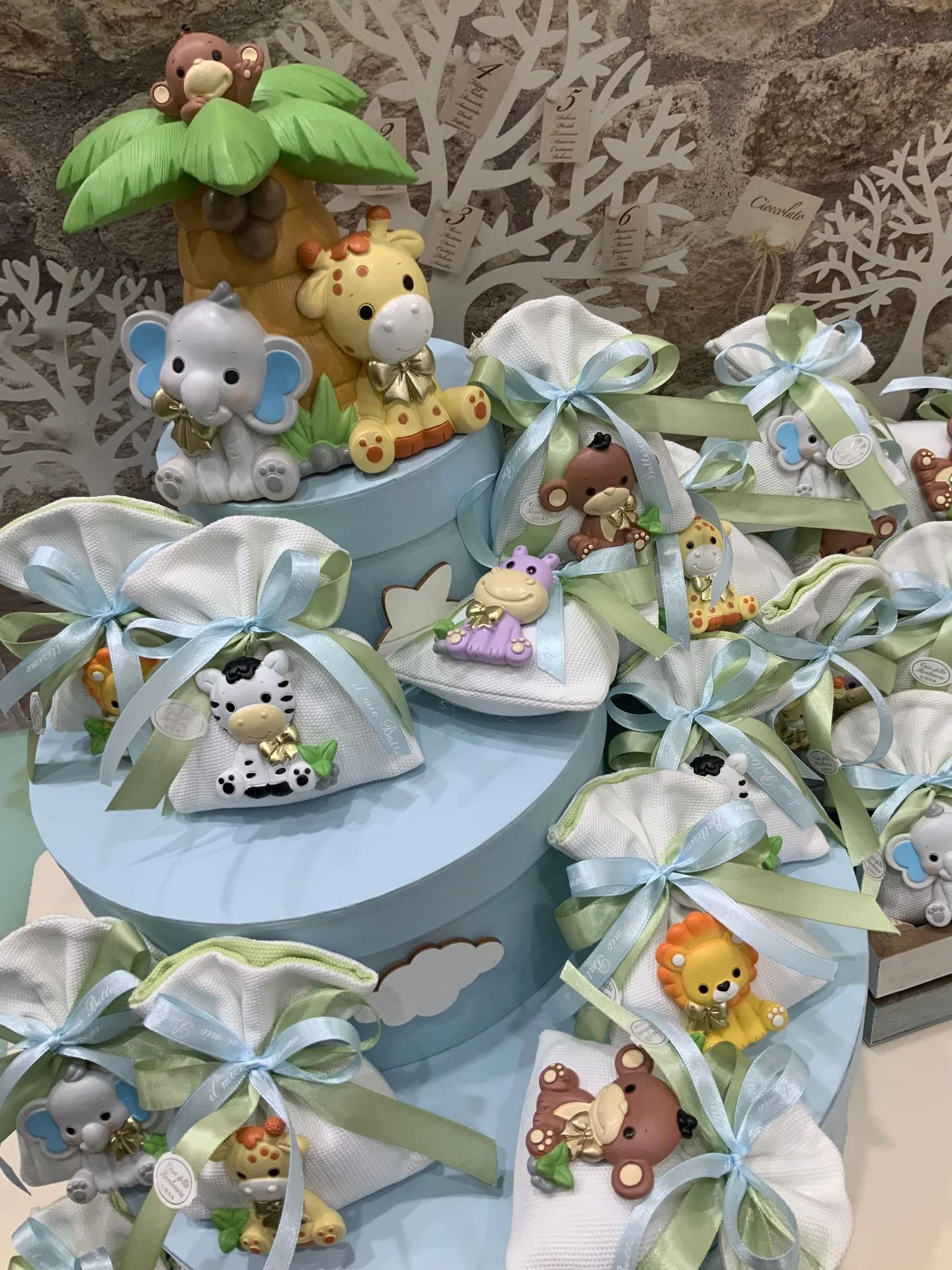 Sacchetti regalo dai colori pastello, legati con nastri e decorati con minuscole statuette di animali su un'alzatina a più livelli, nei toni del menta e del blu.