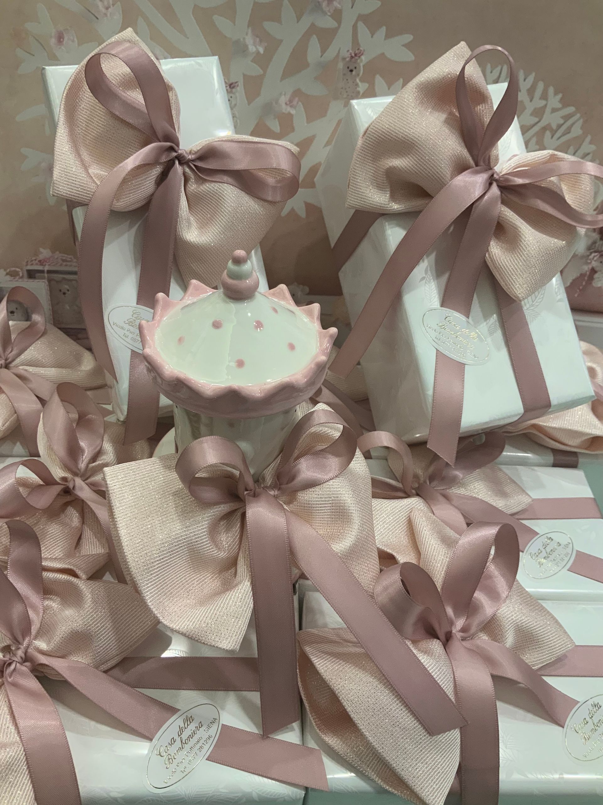 Scatole regalo color pastello con fiocchi rosa e una decorazione a forma di cupcake su uno sfondo a fantasia.