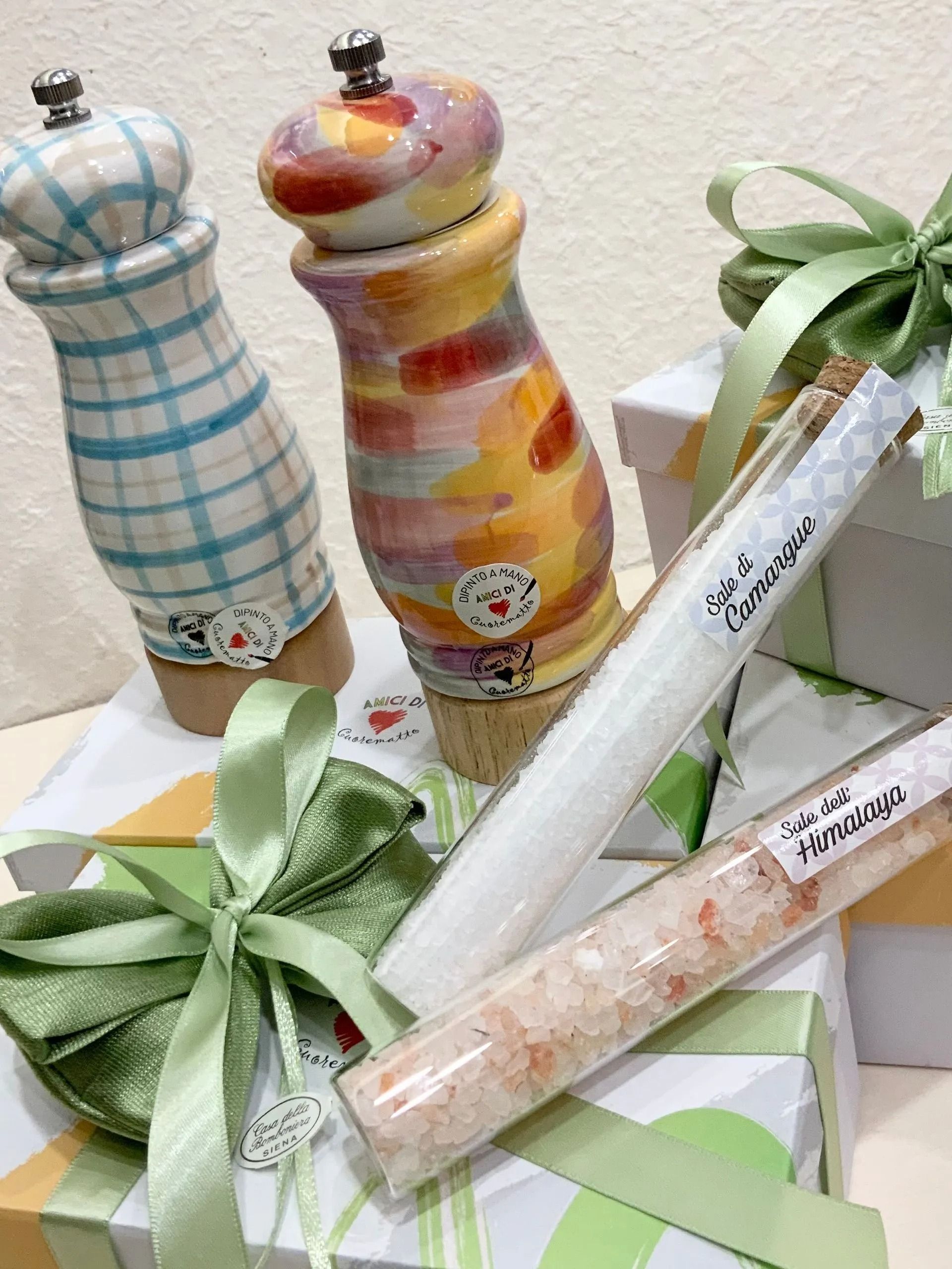 Espositore per set regalo con bottiglie e candele dalle etichette pastello, legate con fiocchi di nastro verde.