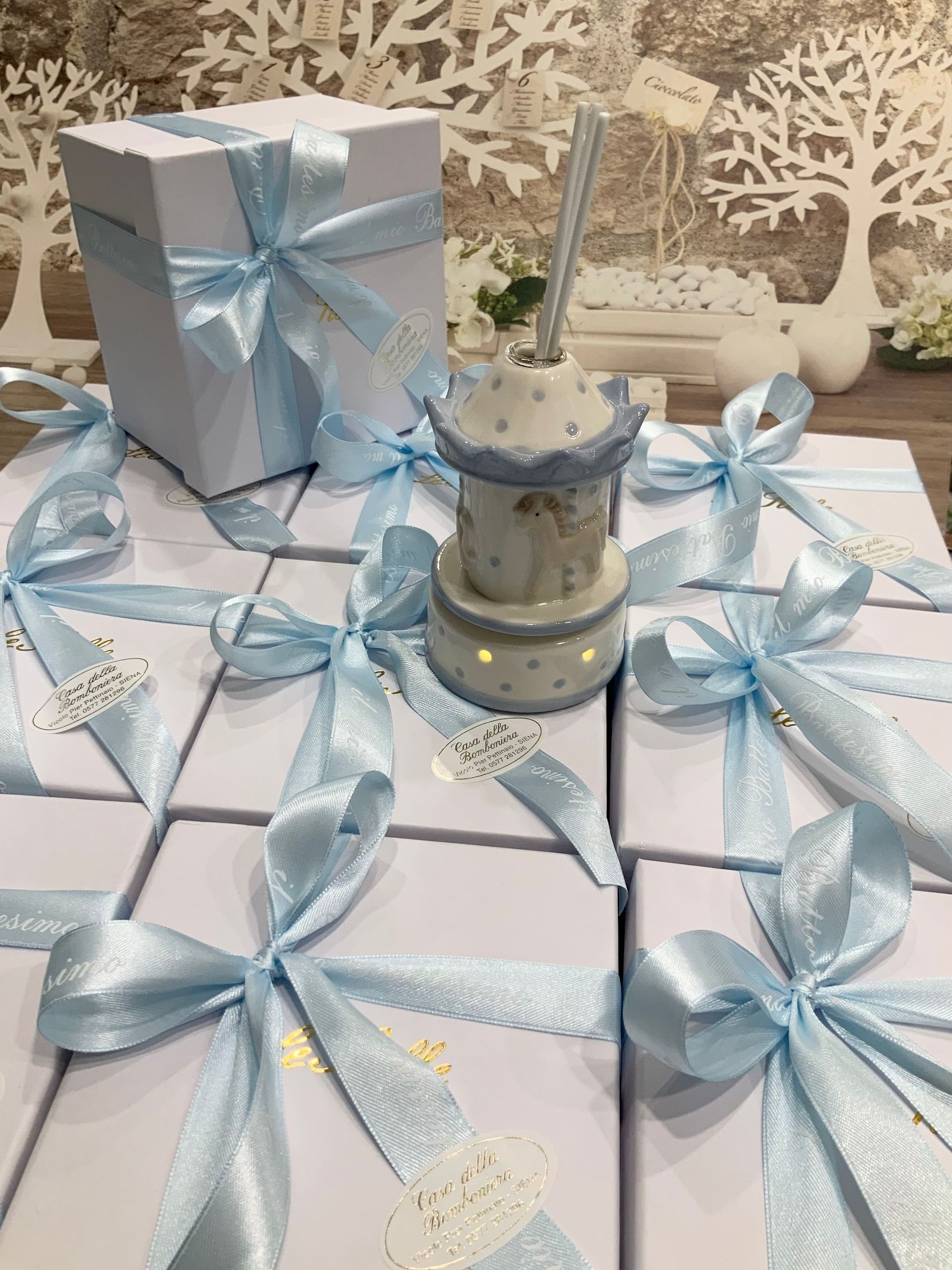 Scatole regalo color azzurro pastello, legate con nastri attorno a un centrotavola con candela decorata.