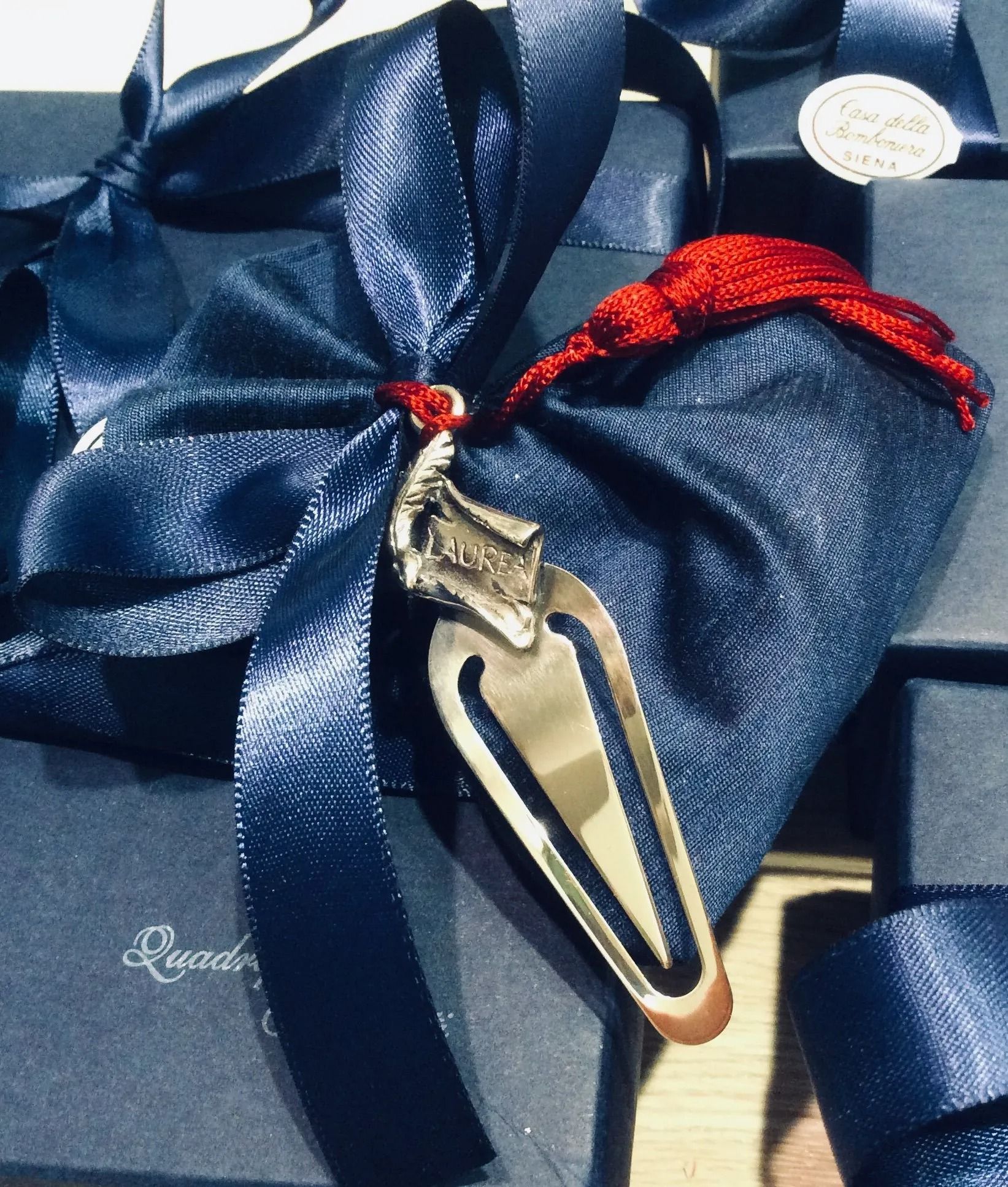 Scatola regalo avvolta in un nastro blu con ciondolo portachiavi oro e nero e cordino rosso decorativo.