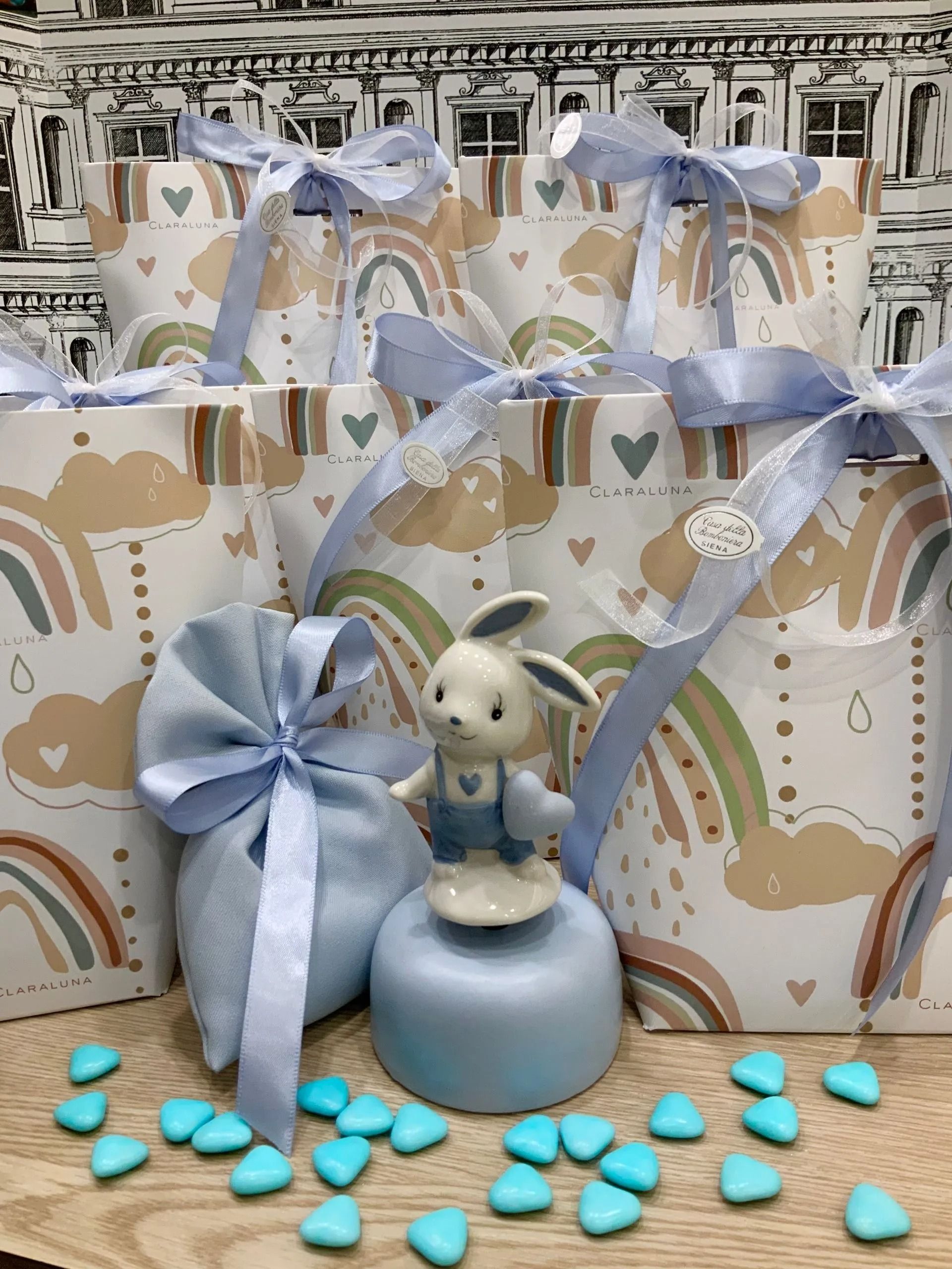 Confezione regalo con nastro blu, piccola statuetta di coniglietto su un piedistallo blu e caramelle blu sparse su un tavolo.