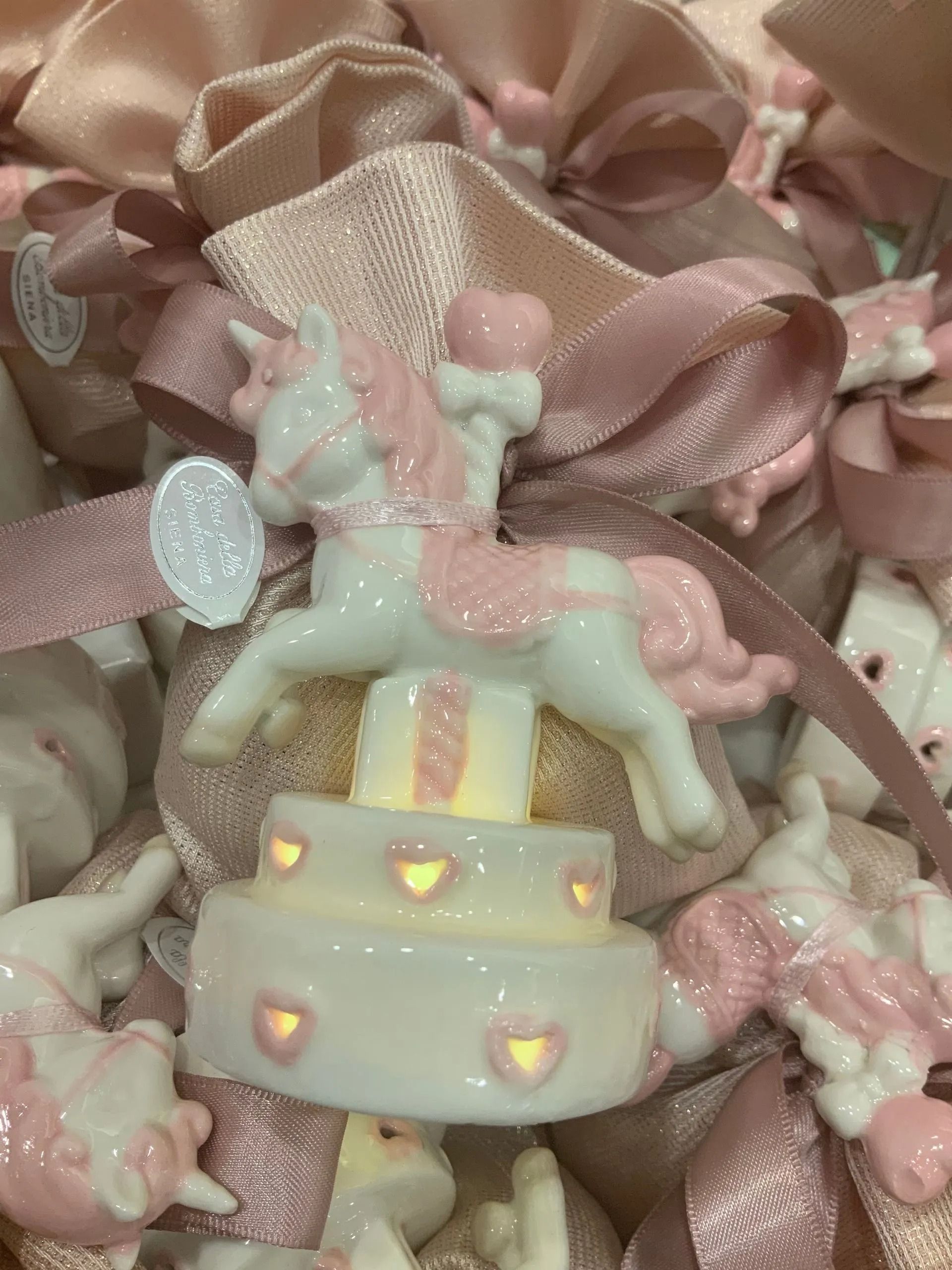 Decorazione per torta a forma di unicorno dai colori pastello su nastro di raso rosa con lucine a forma di cuore.