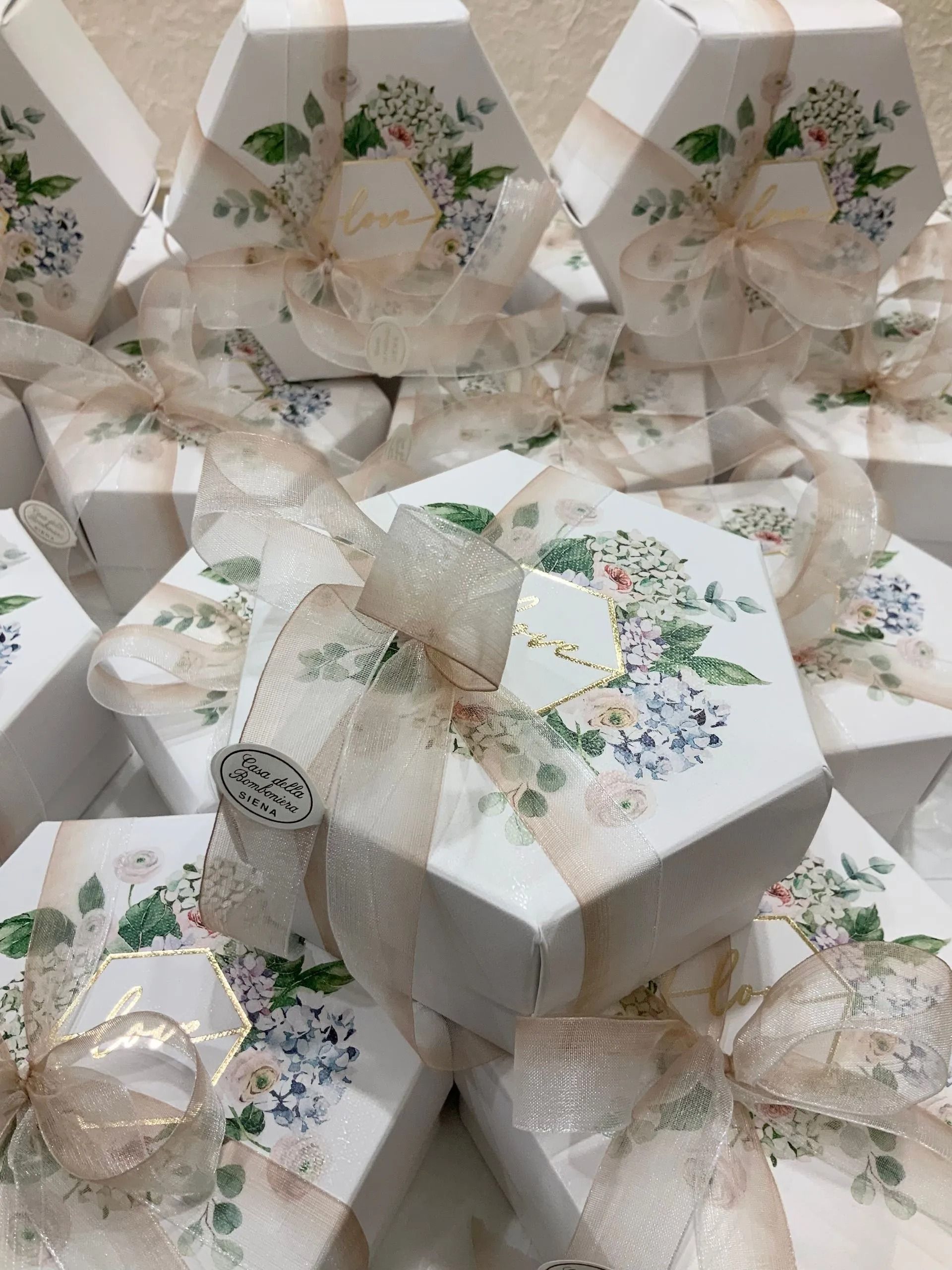 Scatole regalo bianche impilate con stampe floreali e fiocchi di nastro dorato.