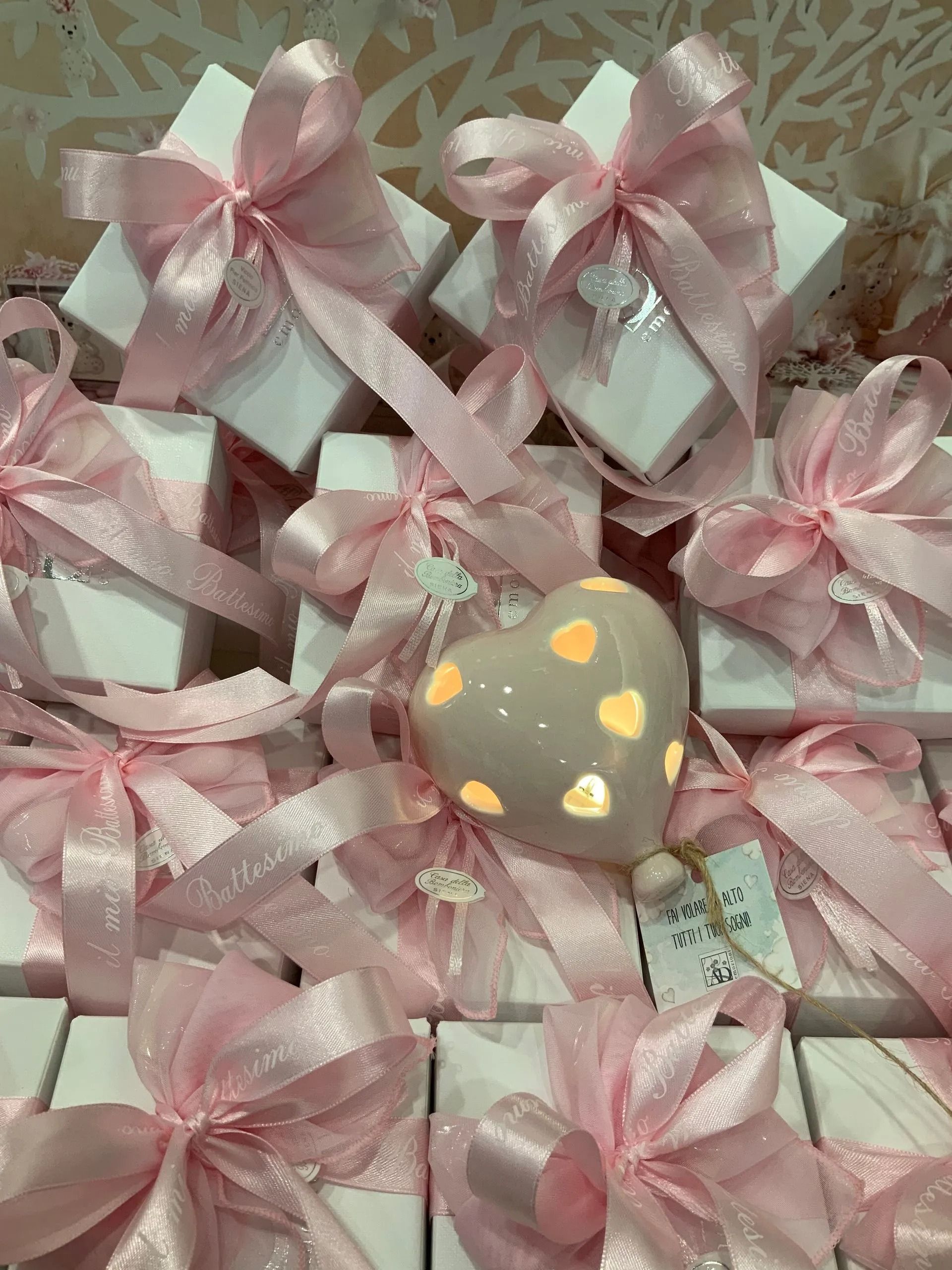 Scatole regalo con nastro rosa e un piccolo biscotto grigio a forma di cuore decorato con cuoricini gialli.