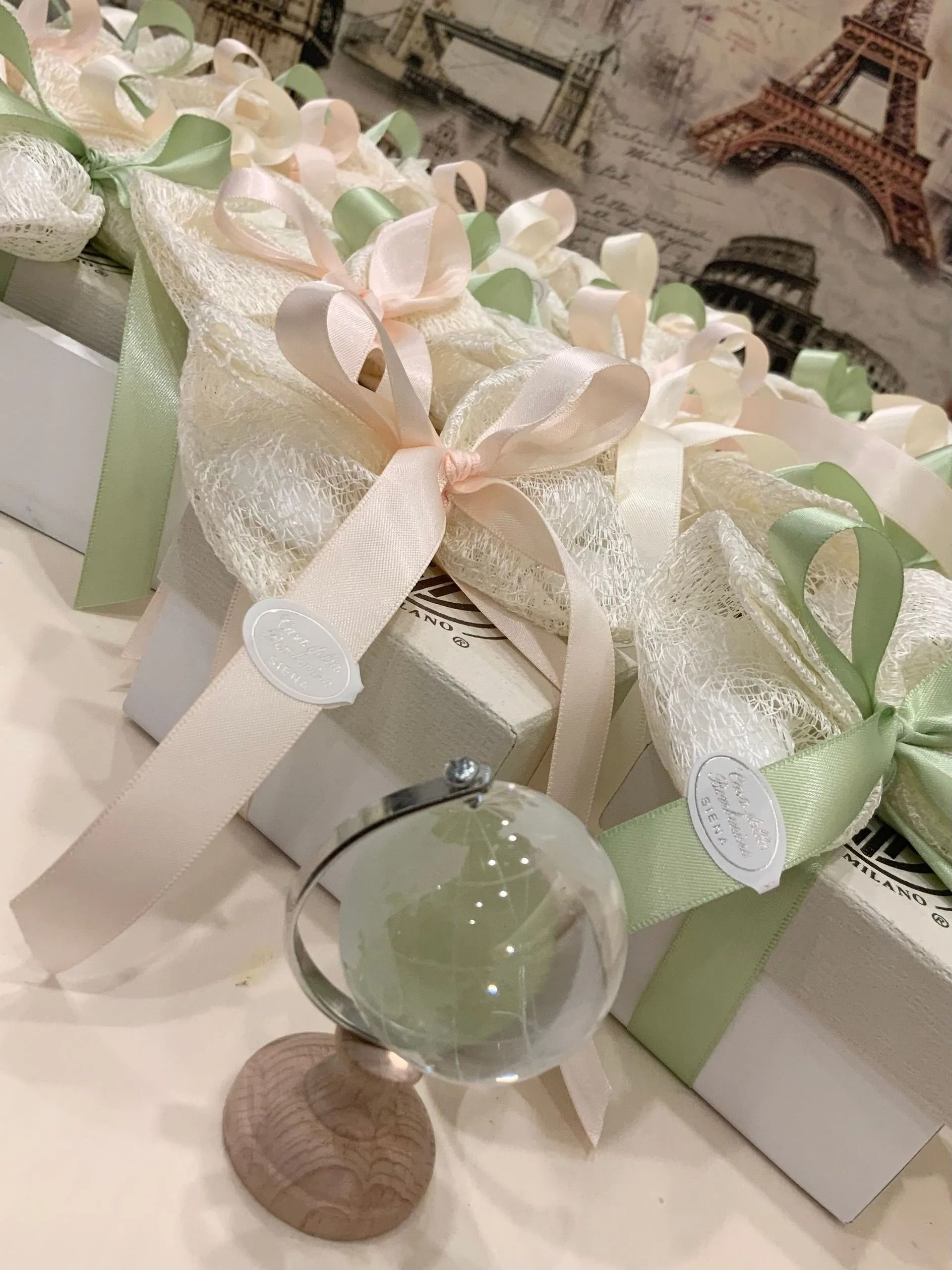 Scatole regalo con fiocchi bianchi e nastro verde, decorate con una piccola Torre Eiffel e un ornamento di cristallo.