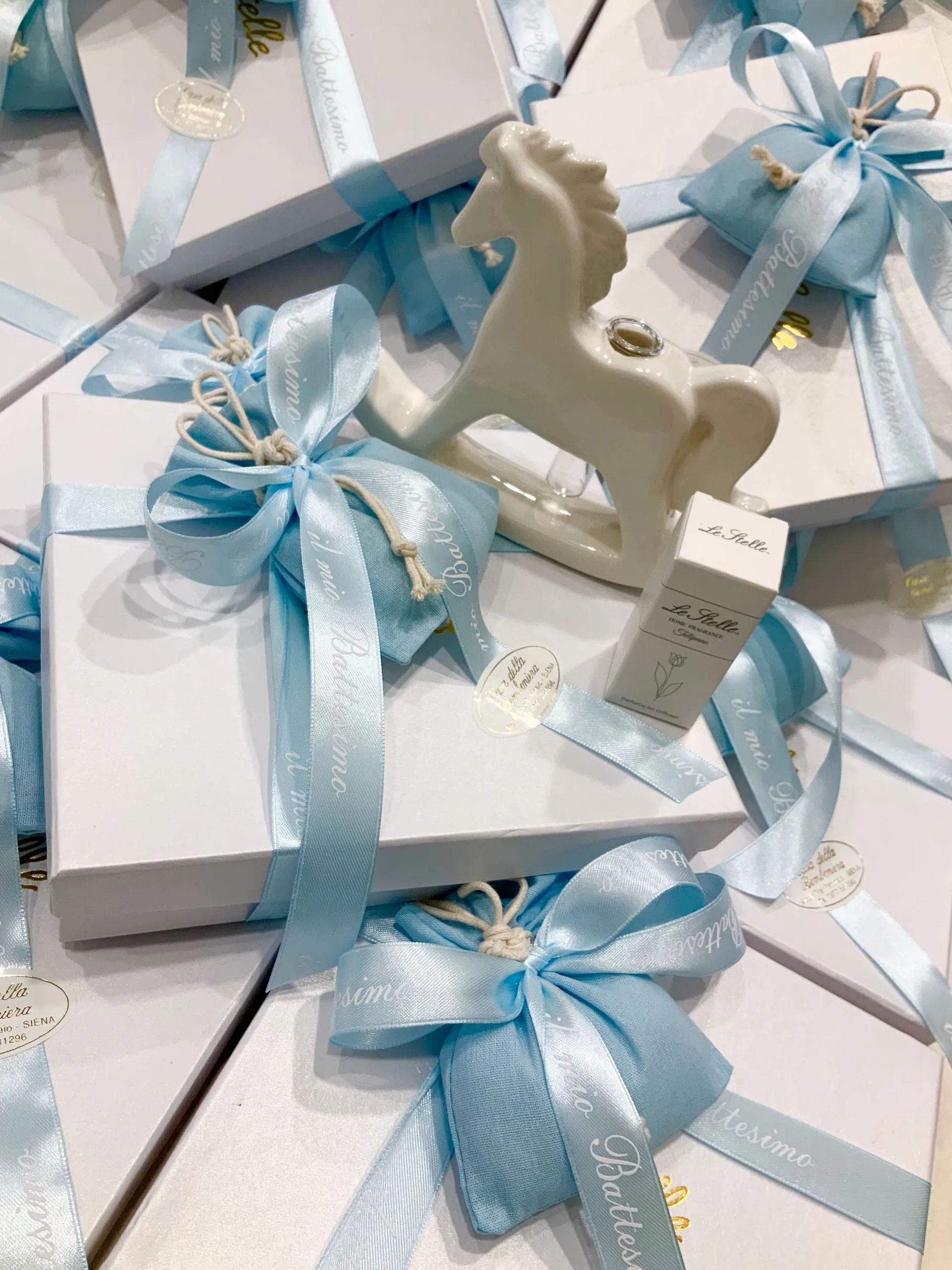 Scatole regalo bianche legate con nastri azzurri e decorate con ornamenti a forma di cavallo a dondolo bianchi.