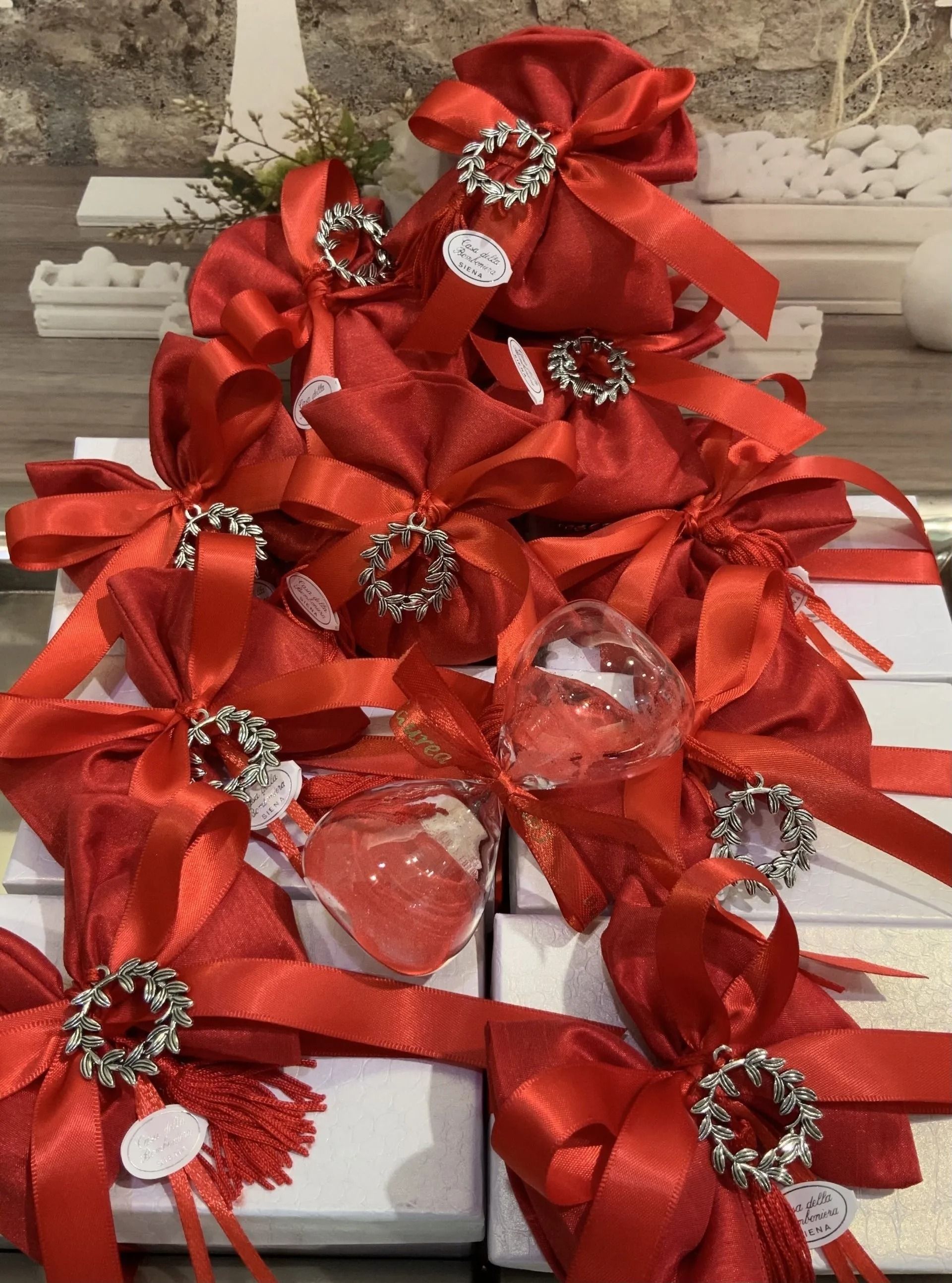 Fiocchi di nastro rosso con ornamenti gioiello disposti su una mensola decorativa bianca.