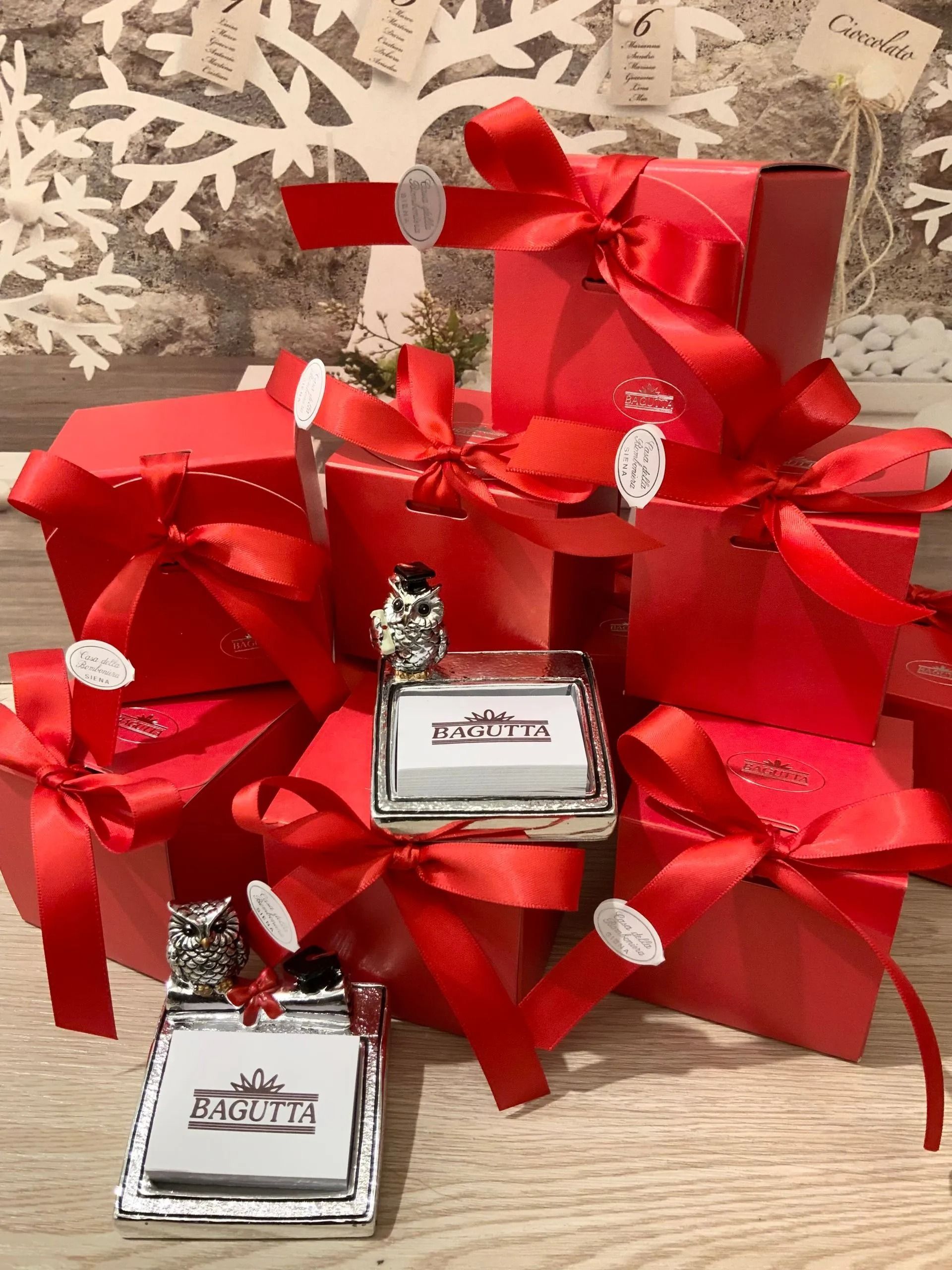 Piccole boccette di profumo argentate con fiocchi rossi e confezione regalo in nastro, disposte su un tavolo.