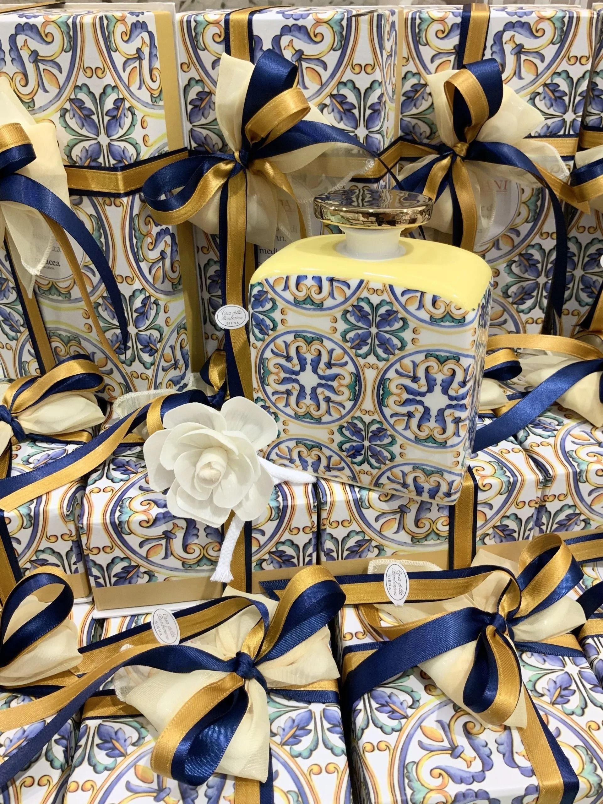 Scatole regalo decorate blu e oro e candele disposte con nastro blu navy e una rosa bianca