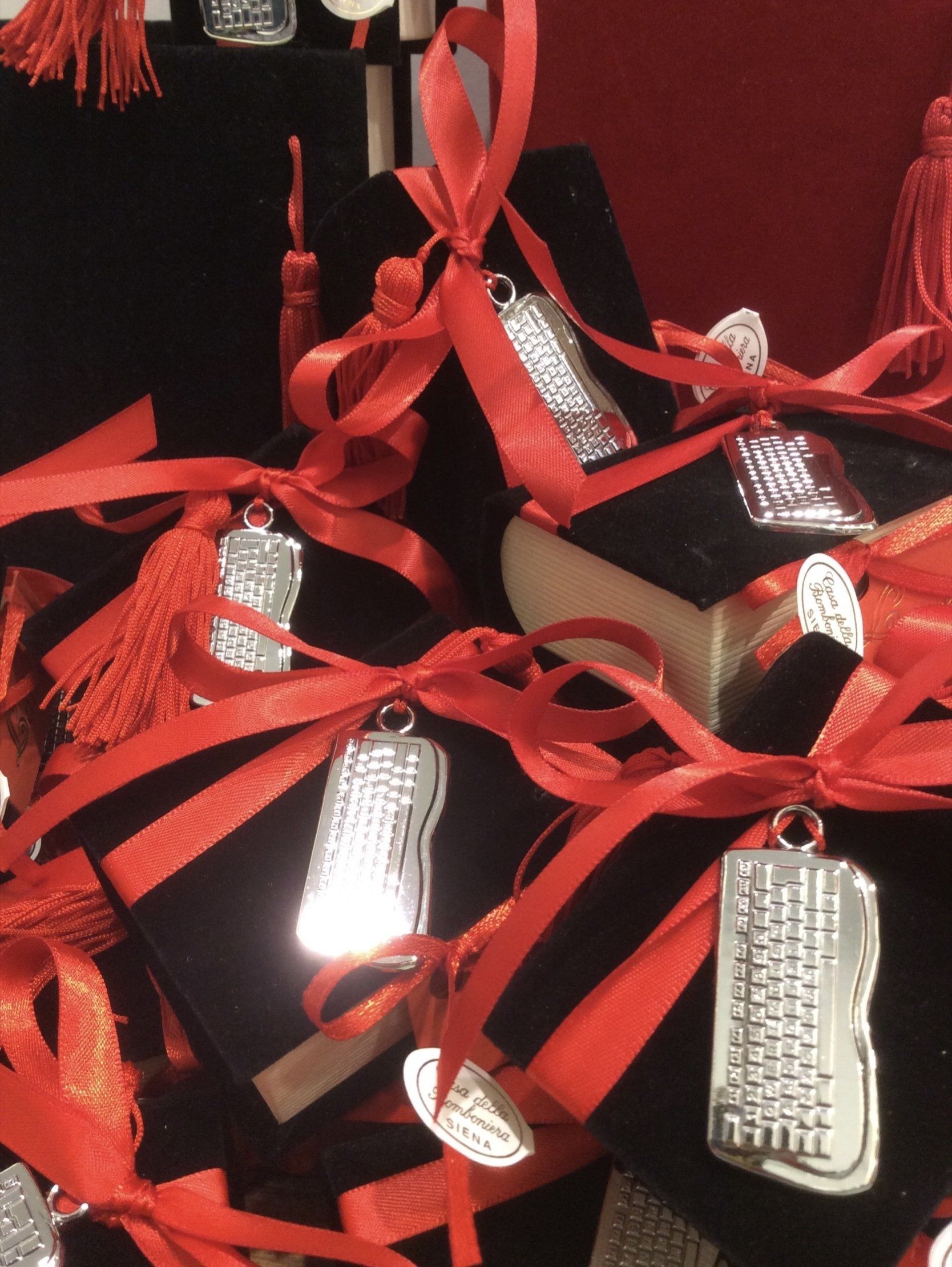 Fiocchi di nastro rosso con etichette regalo argentate su scatole nere, con nappe rosse sullo sfondo.