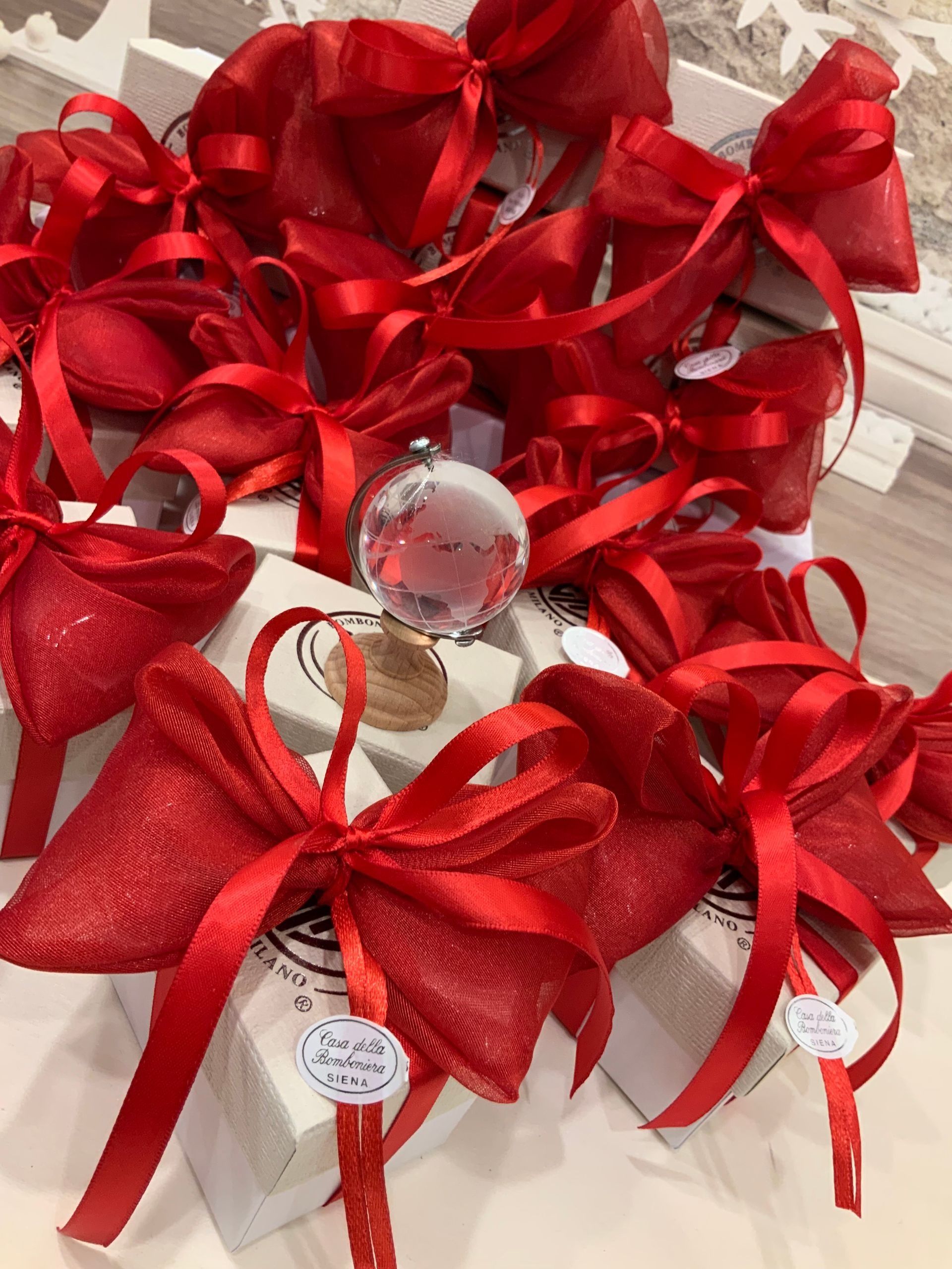 Sacchetti regalo con nastro rosso, fiocchi e cartellini trasparenti disposti su un tavolo
