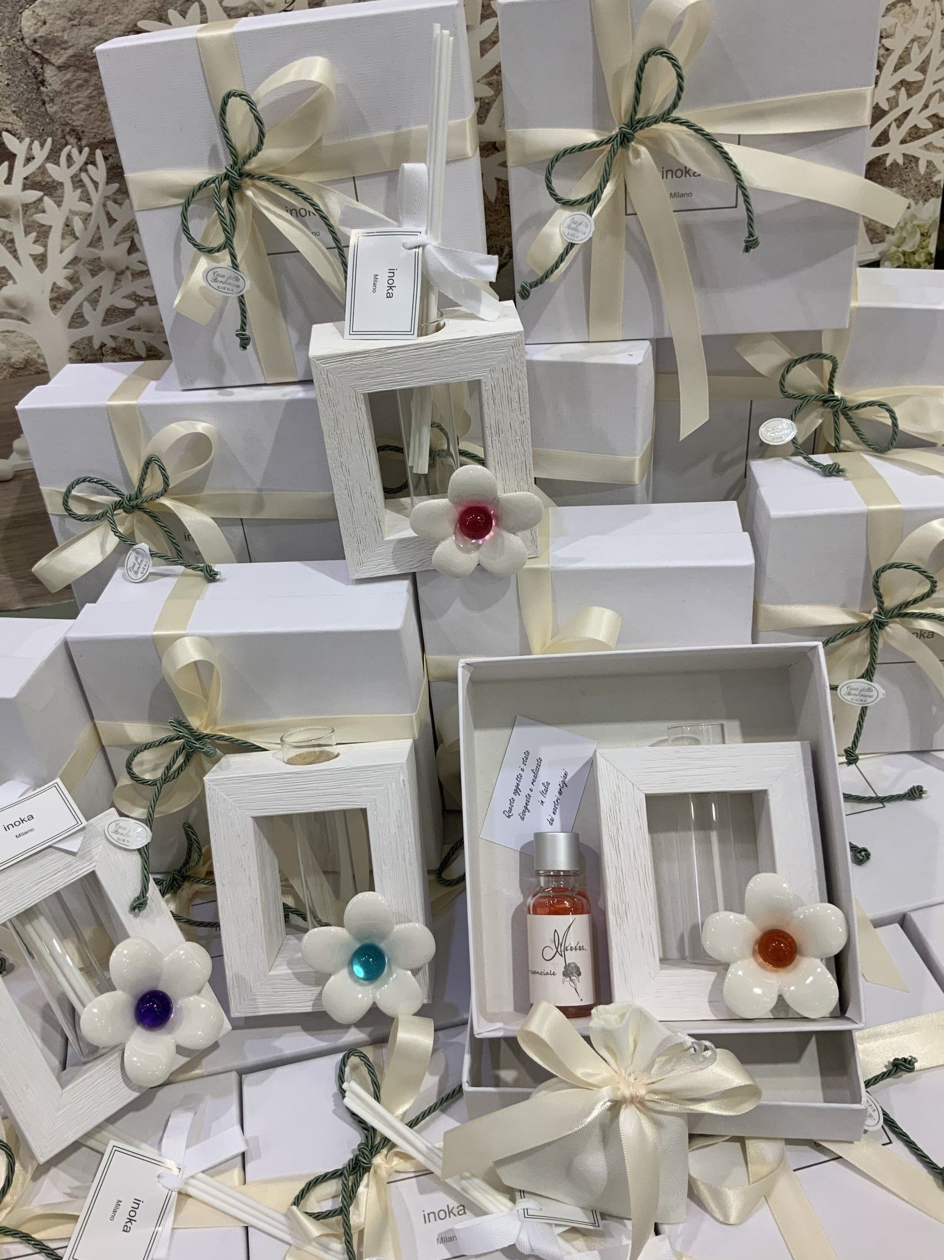 Scatole regalo bianche e minuscoli ornamenti incorniciati con nastri argentati e fiorellini colorati disposti in mostra.