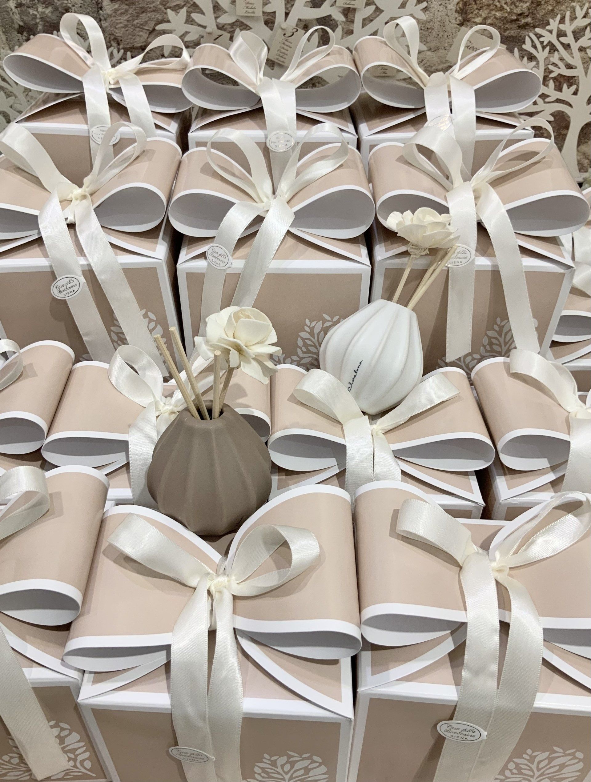 File di scatole regalo beige legate con nastri di raso bianco e decorate con piccoli elementi floreali.