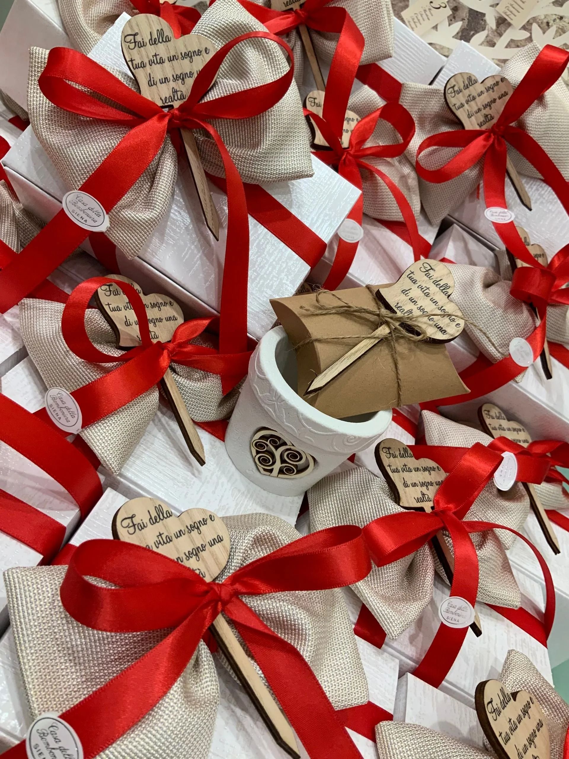 Scatole regalo assortite, avvolte in carta beige con nastri e fiocchi di raso rosso.