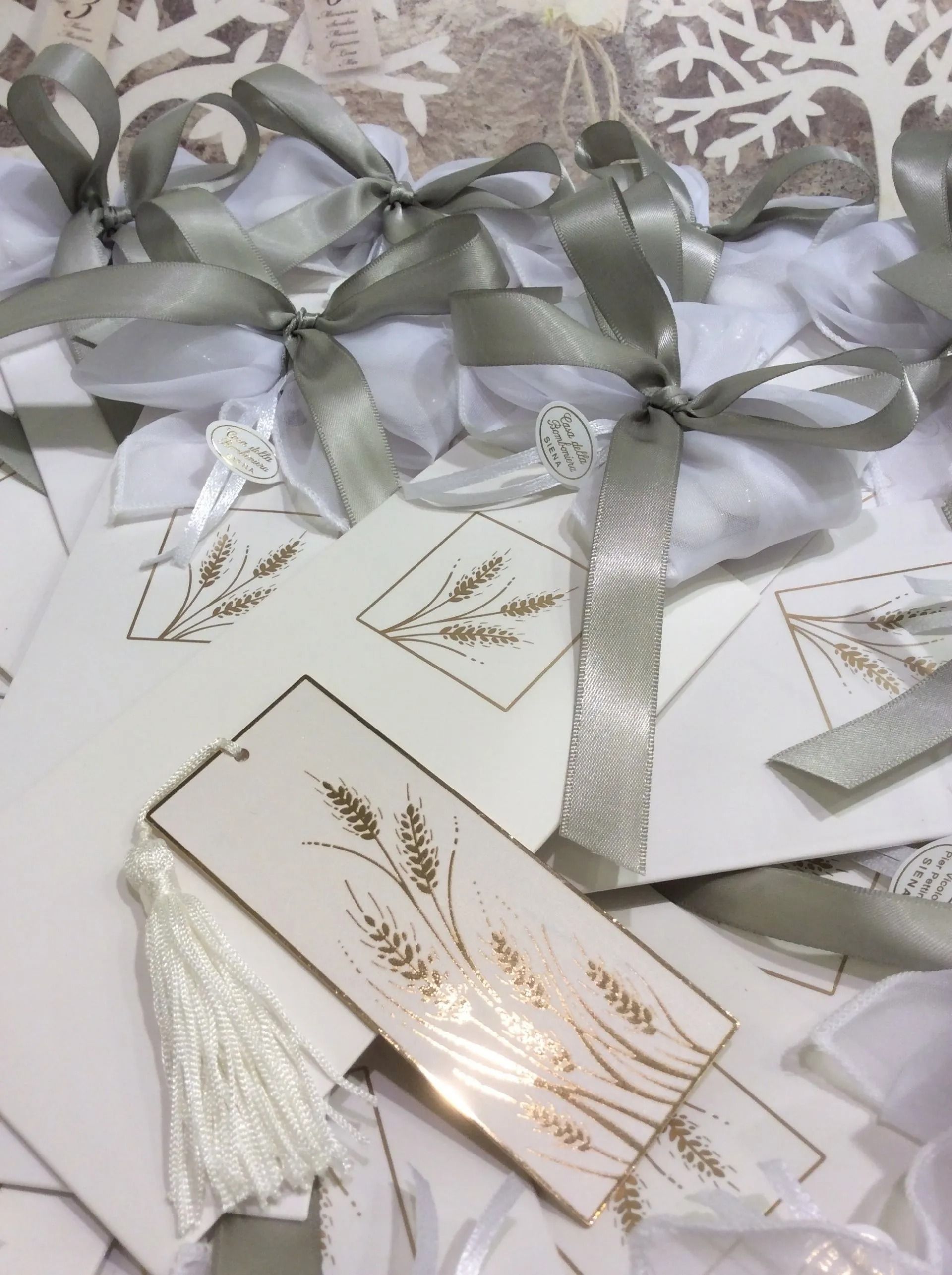 Etichette regalo bianche con decorazioni in foglia d'oro e fiocchi in nastro argentato su sfondo fantasia.