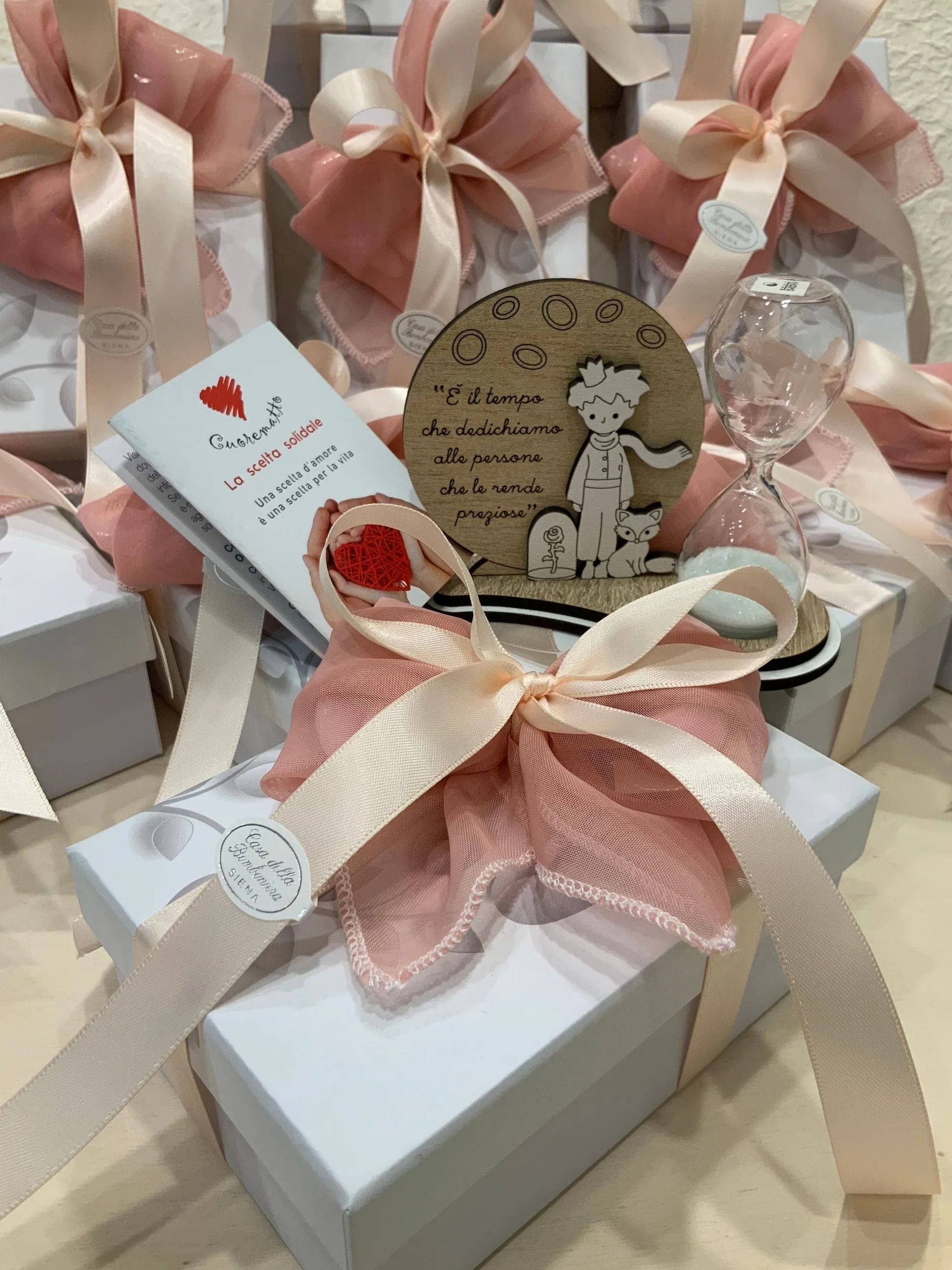 Scatole regalo avvolte in un nastro rosa e bianco, con etichette decorative e piccoli ornamenti.