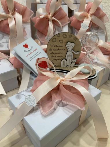 Scatole regalo avvolte in un nastro rosa e bianco, con etichette decorative e piccoli ornamenti.