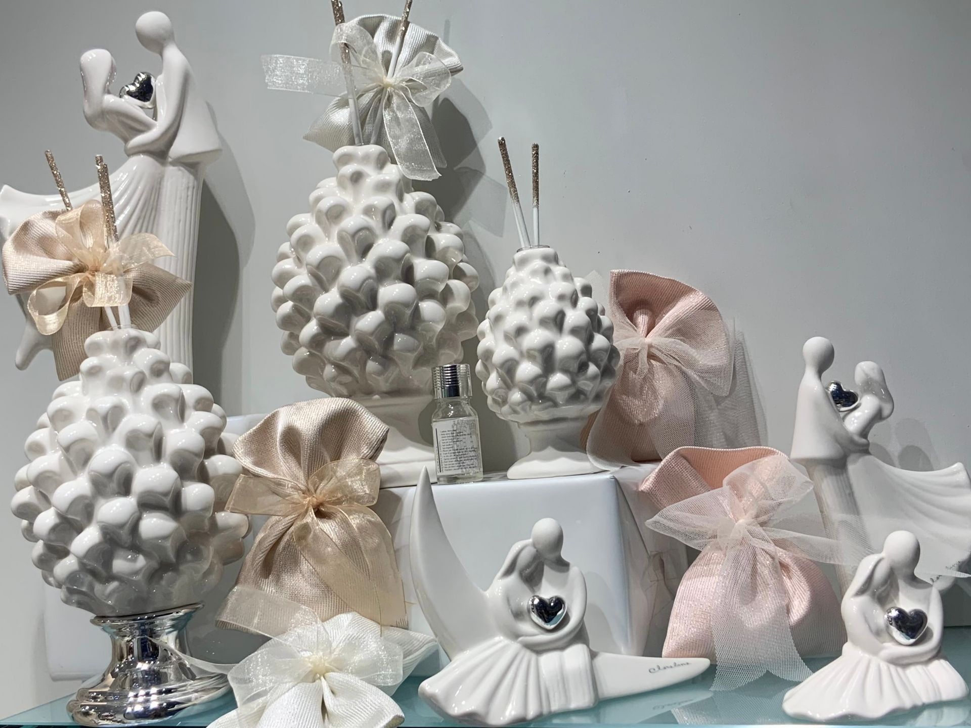 Statuette e ornamenti natalizi decorativi bianchi e pastello disposti su uno scaffale espositivo.