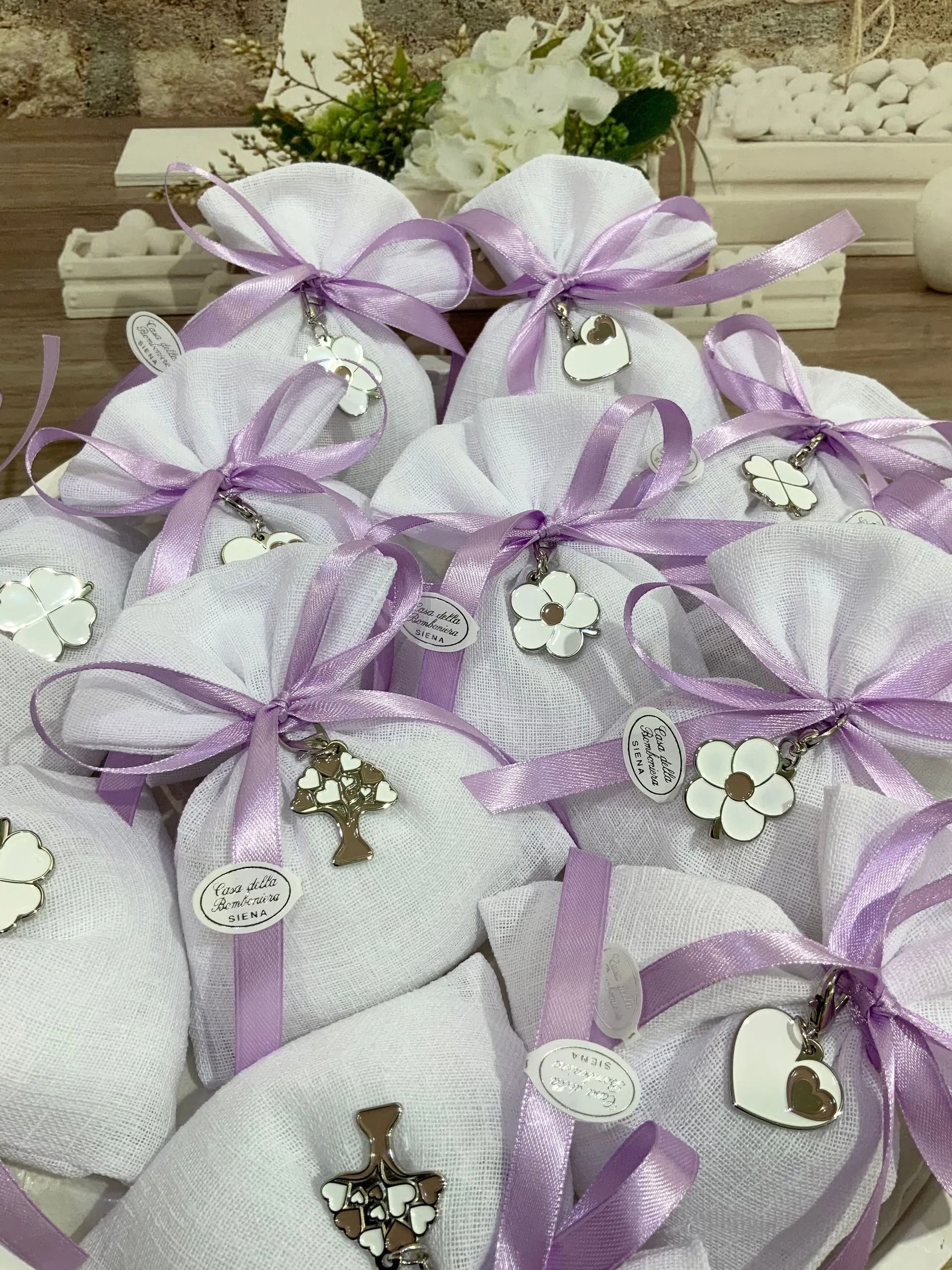 Sacchetti regalo in organza lilla disposti in un cestino, decorati con fiori bianchi e argento.