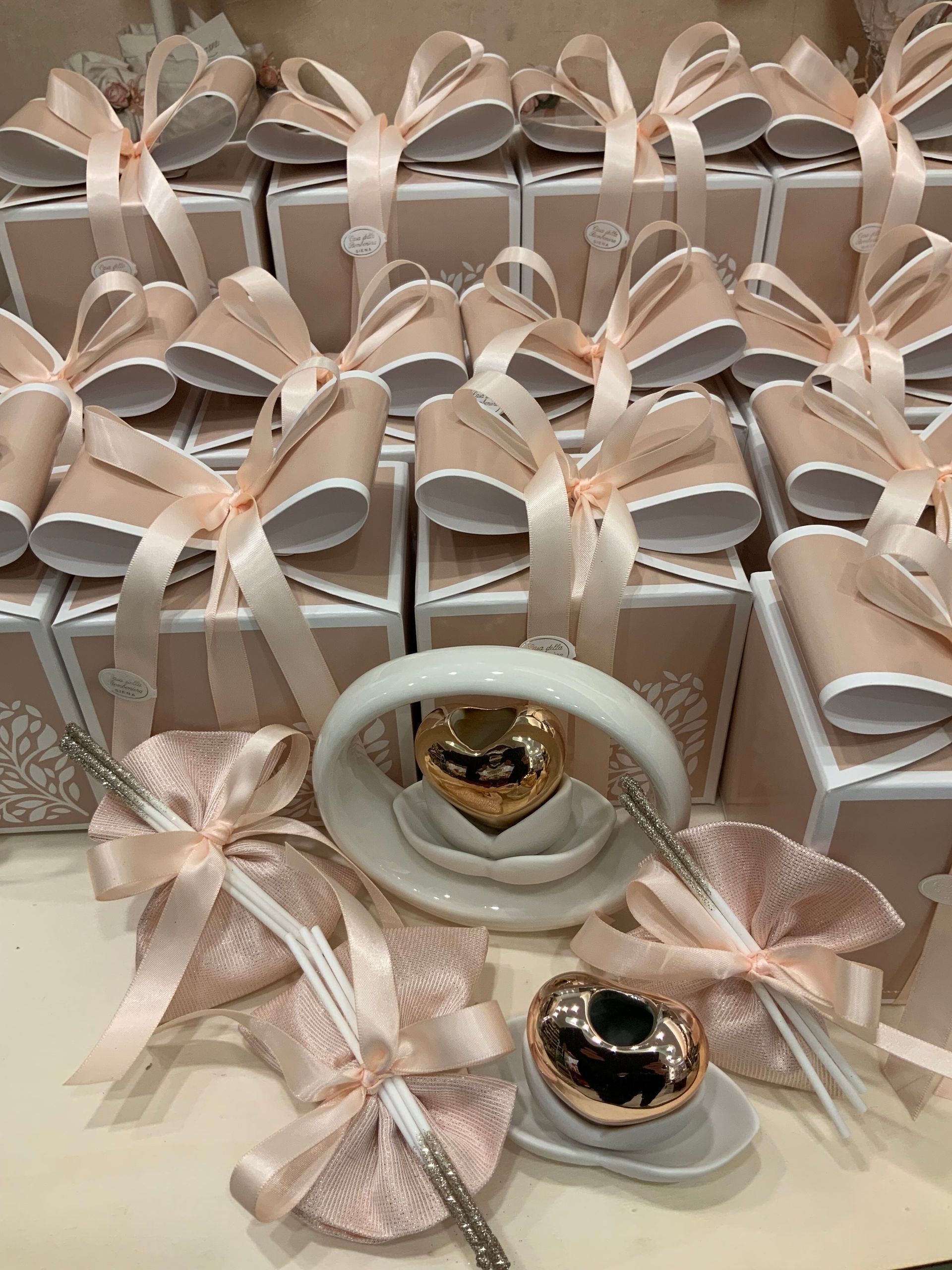 Scatole regalo rosa pastello con fiocchi di nastro, disposte dietro un espositore bianco per anelli con due anelli gioiello