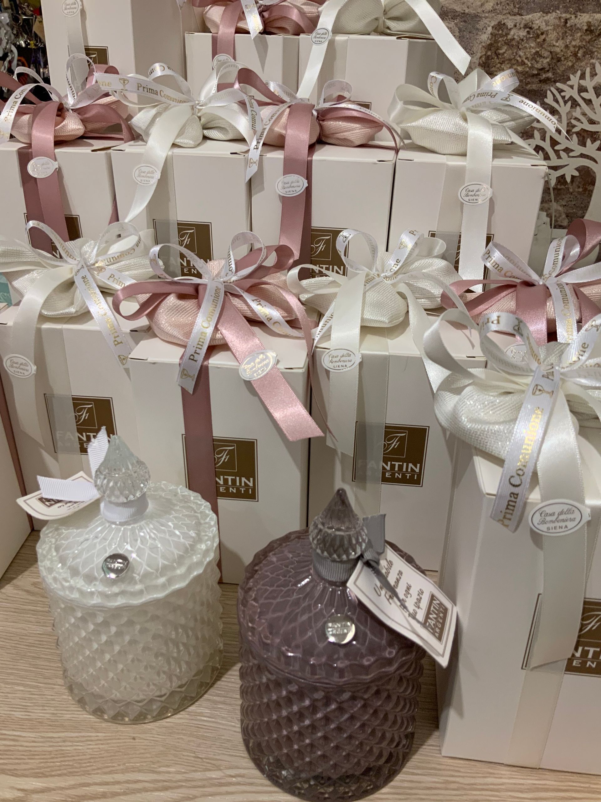Sacchetti regalo decorativi con nastri rosa e vasetti di candele scintillanti nei colori bianco e viola.