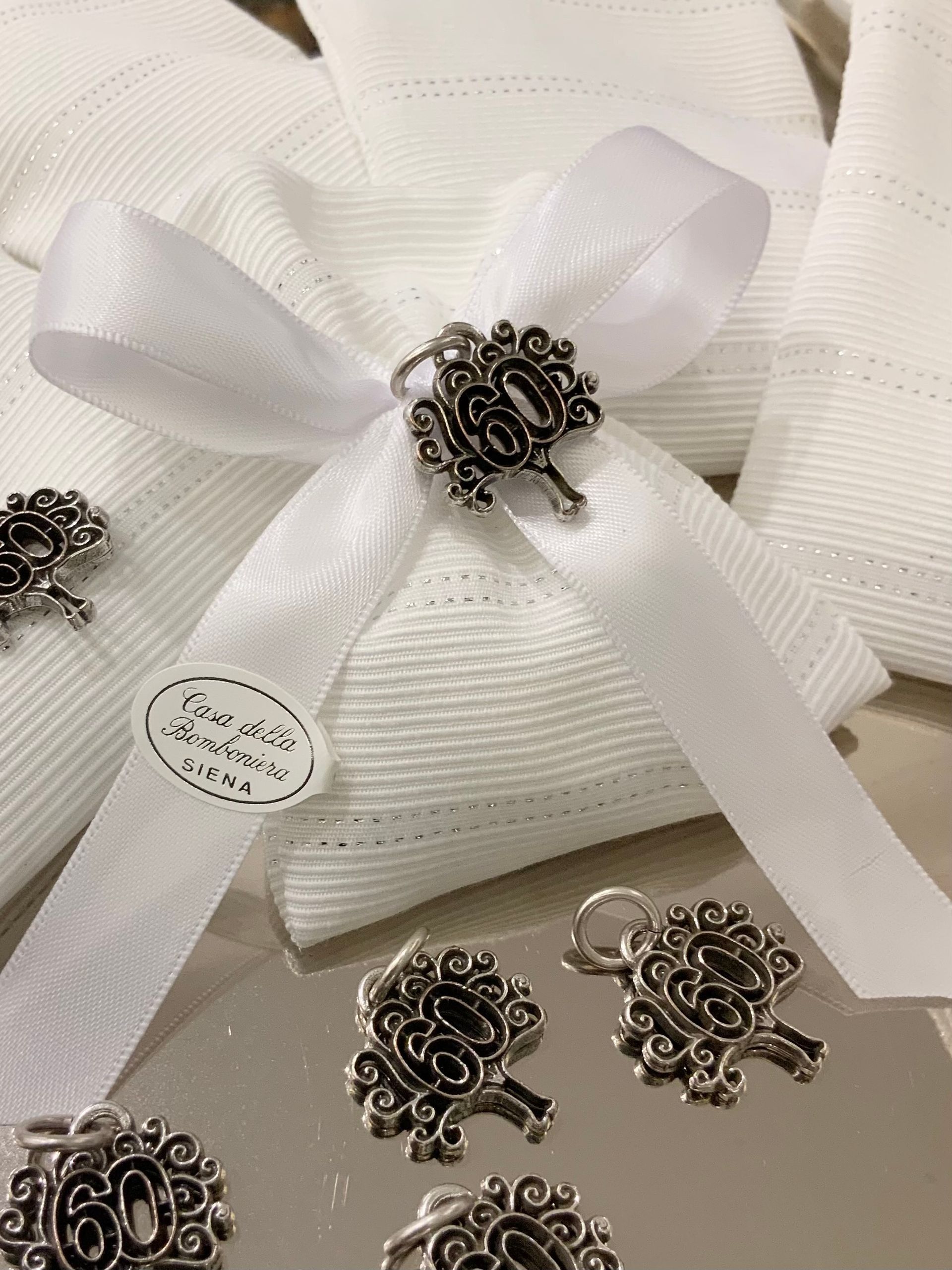 Scatola regalo bianca con texture, decorata con nastro e spille o ciondoli argentati sulla parte superiore.