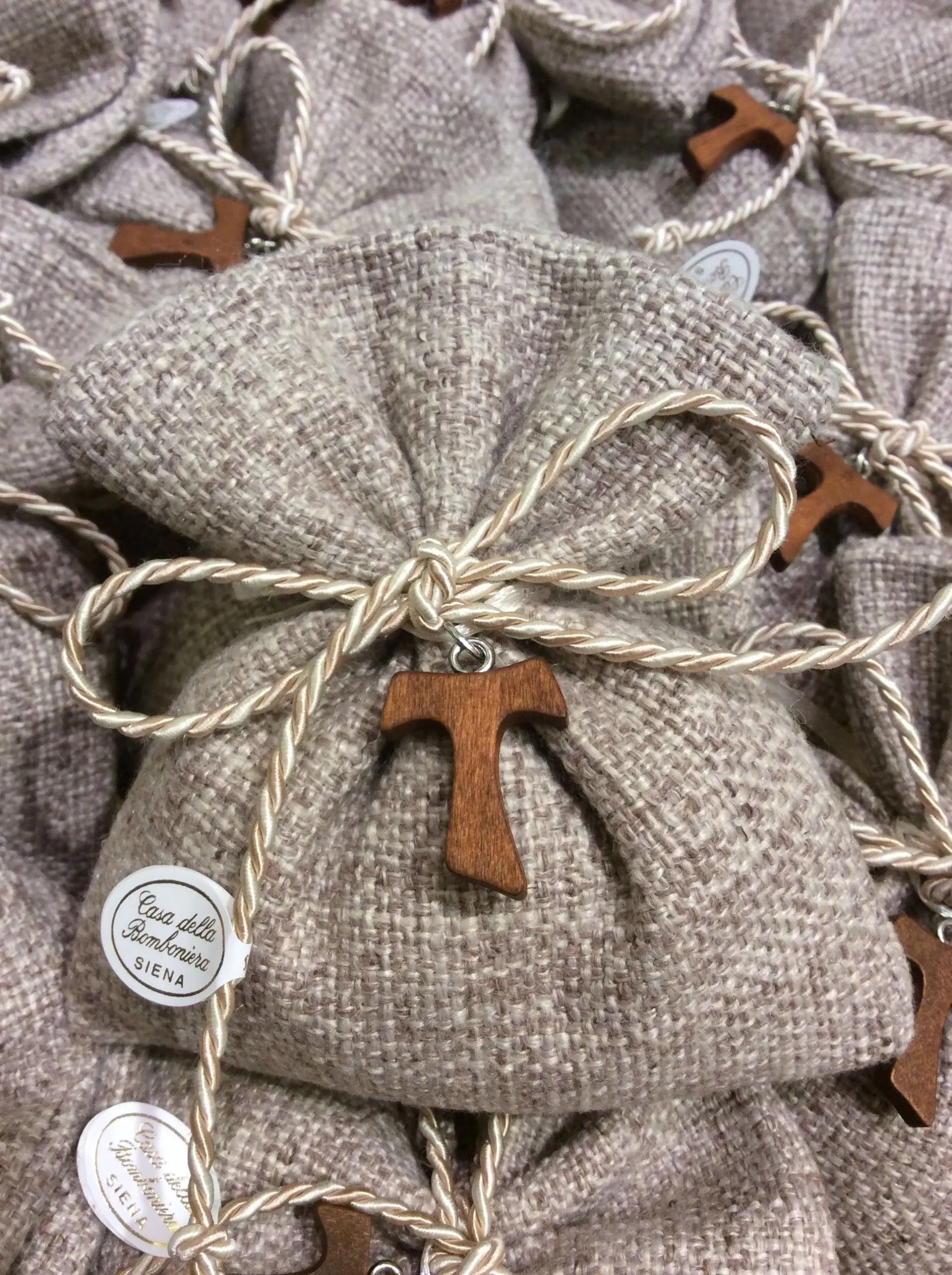 Sacchetti regalo in lino grigio, legati con spago e targhette di legno a forma di T, impilati uno sull'altro.