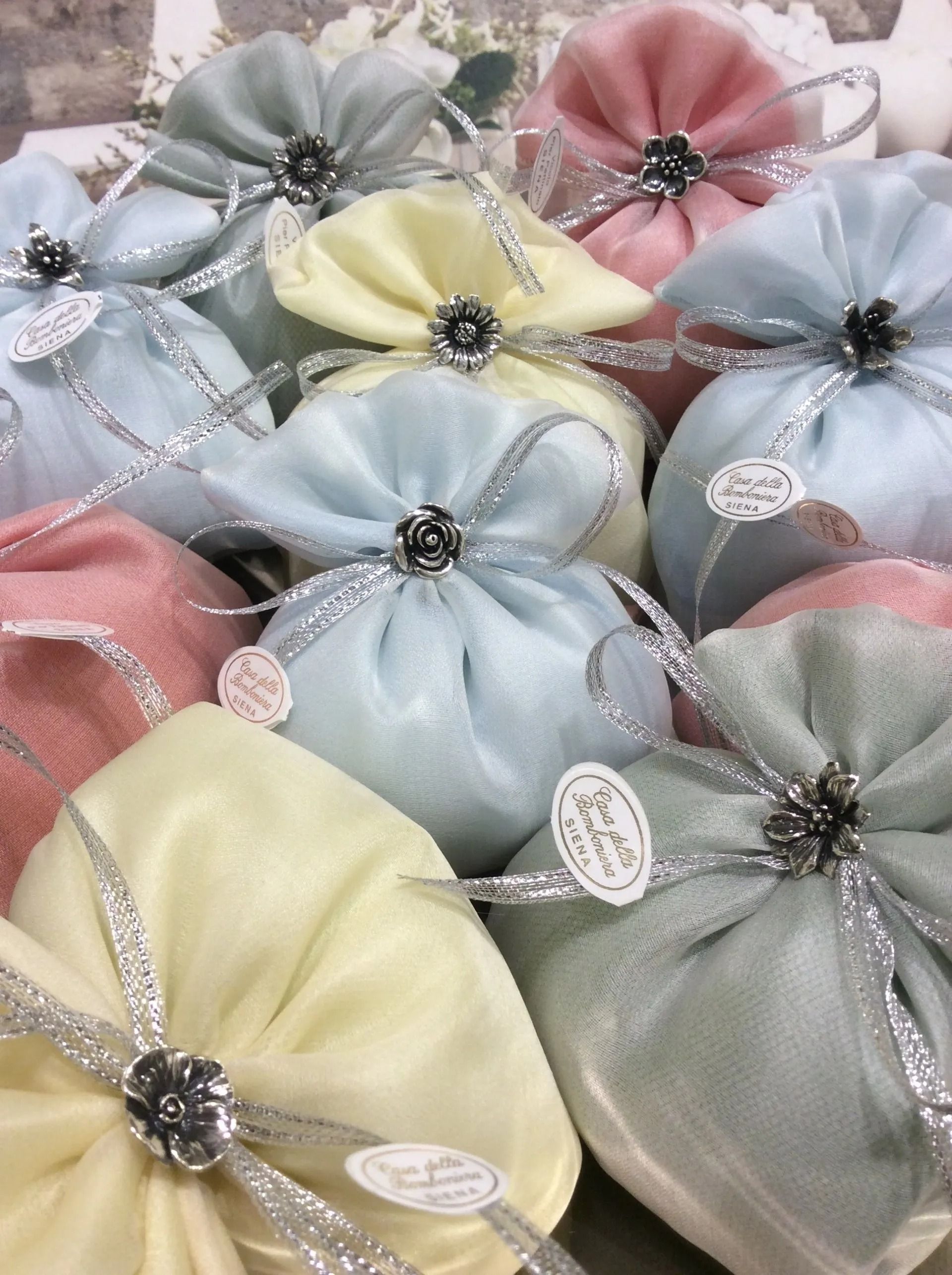 Sacchetti regalo in raso color pastello con nastri argentati e centri gioiello nei colori rosa, blu, verde e giallo.