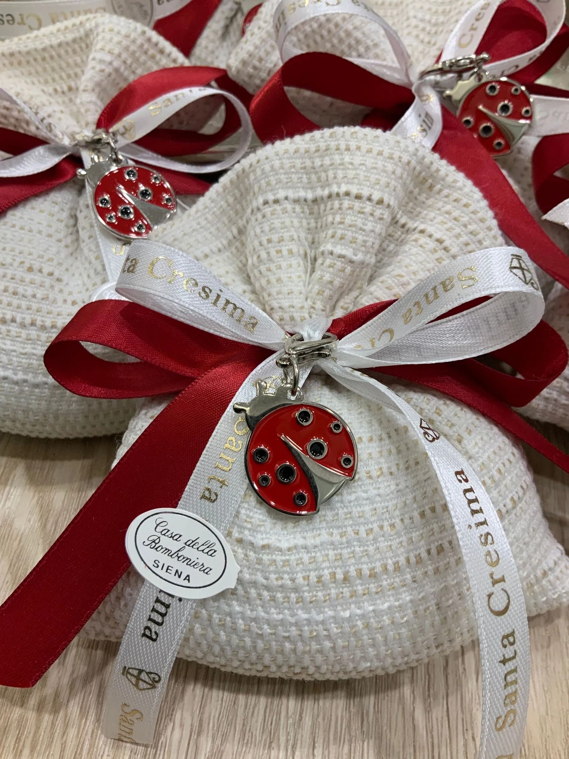 Sacchetti decorativi in ​​tessuto bianco, legati con nastri rossi e bianchi, ognuno con un piccolo ciondolo a forma di coccinella rossa.