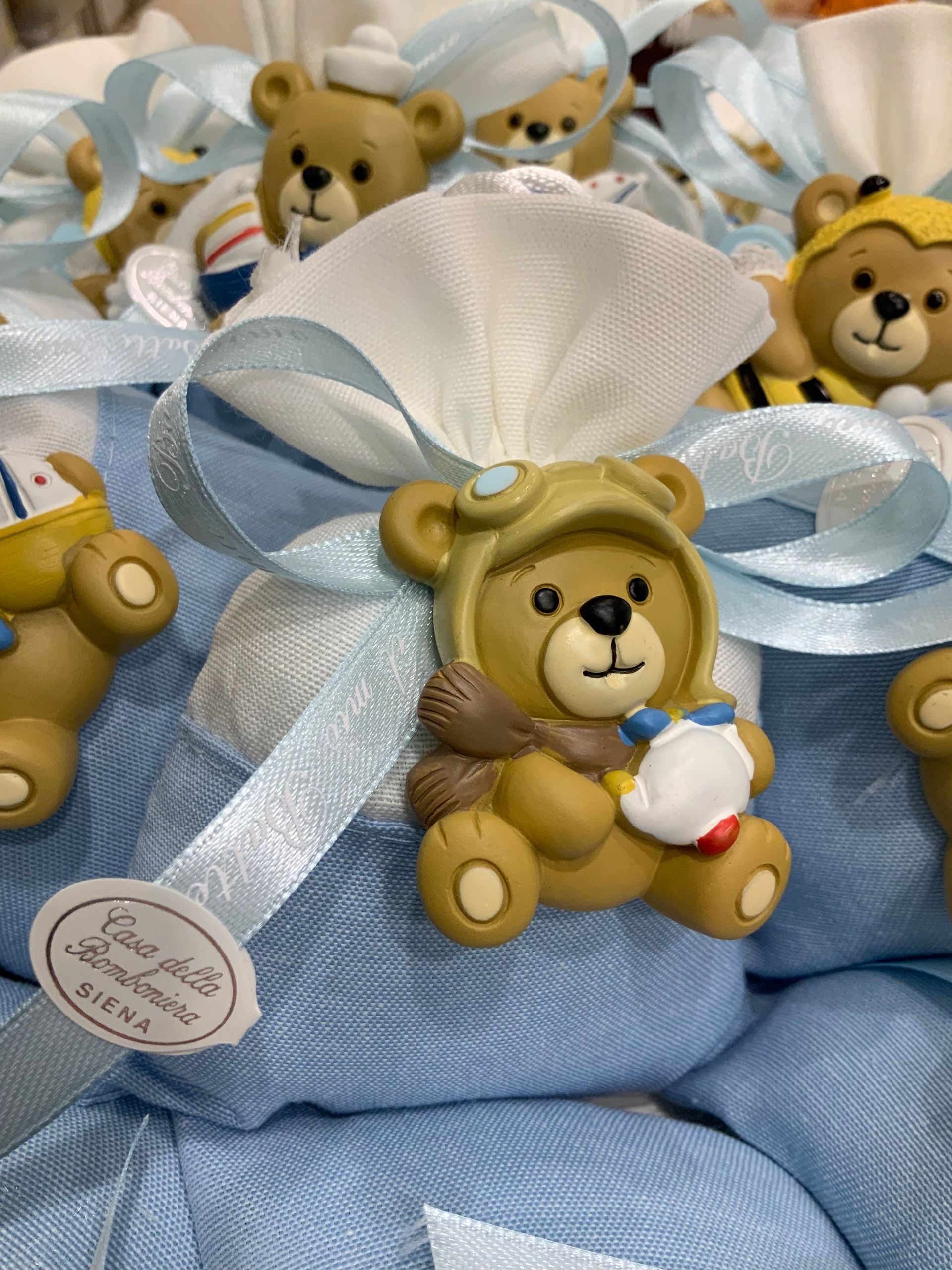 Sacchetti regalo blu decorati con orsetti di peluche e nastri bianchi, con statuette di orsetti di peluche in cima.
