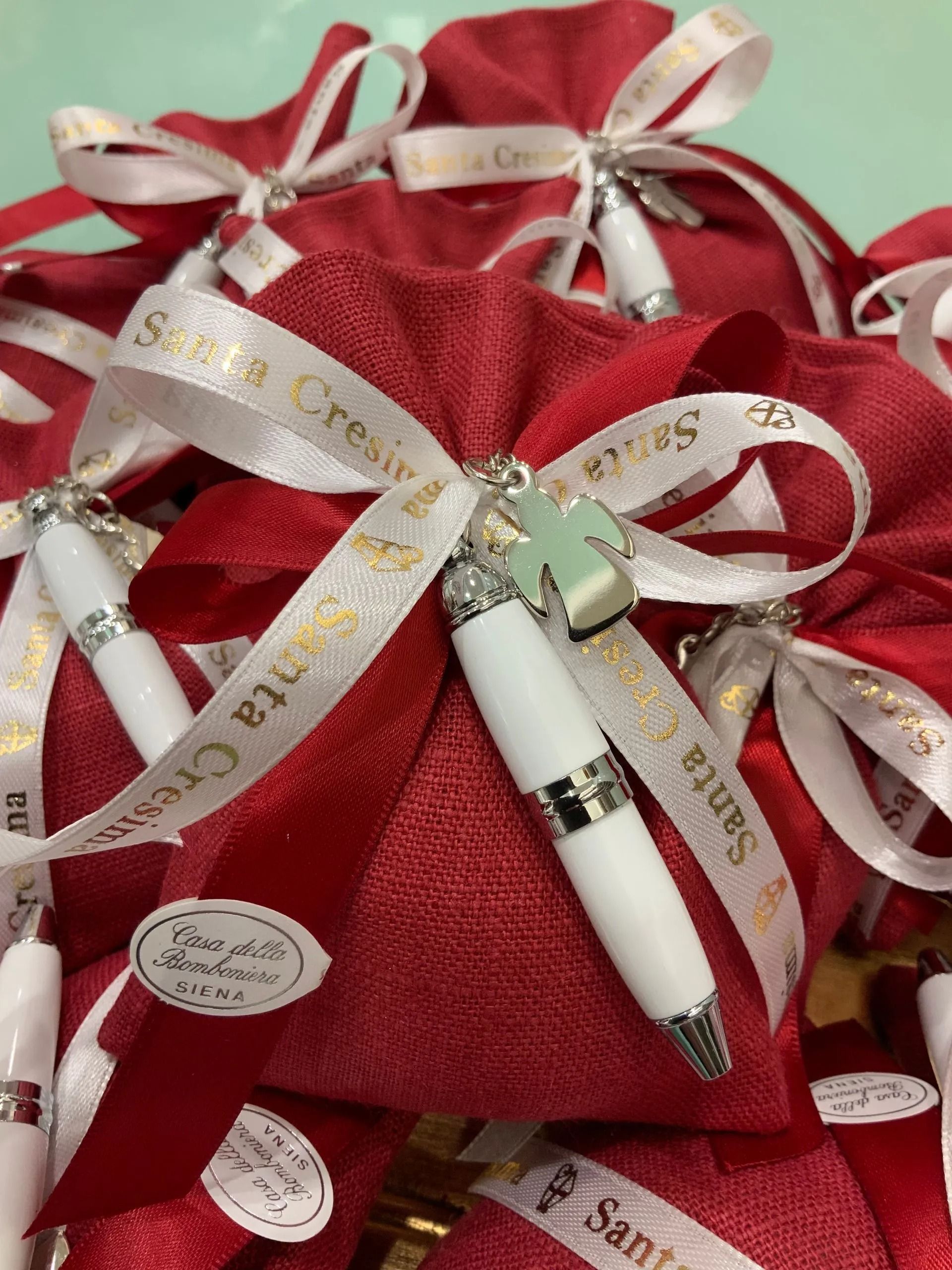 Sacchetti regalo rossi con fiocchi di nastro bianco e oro e bomboniere a forma di penna.