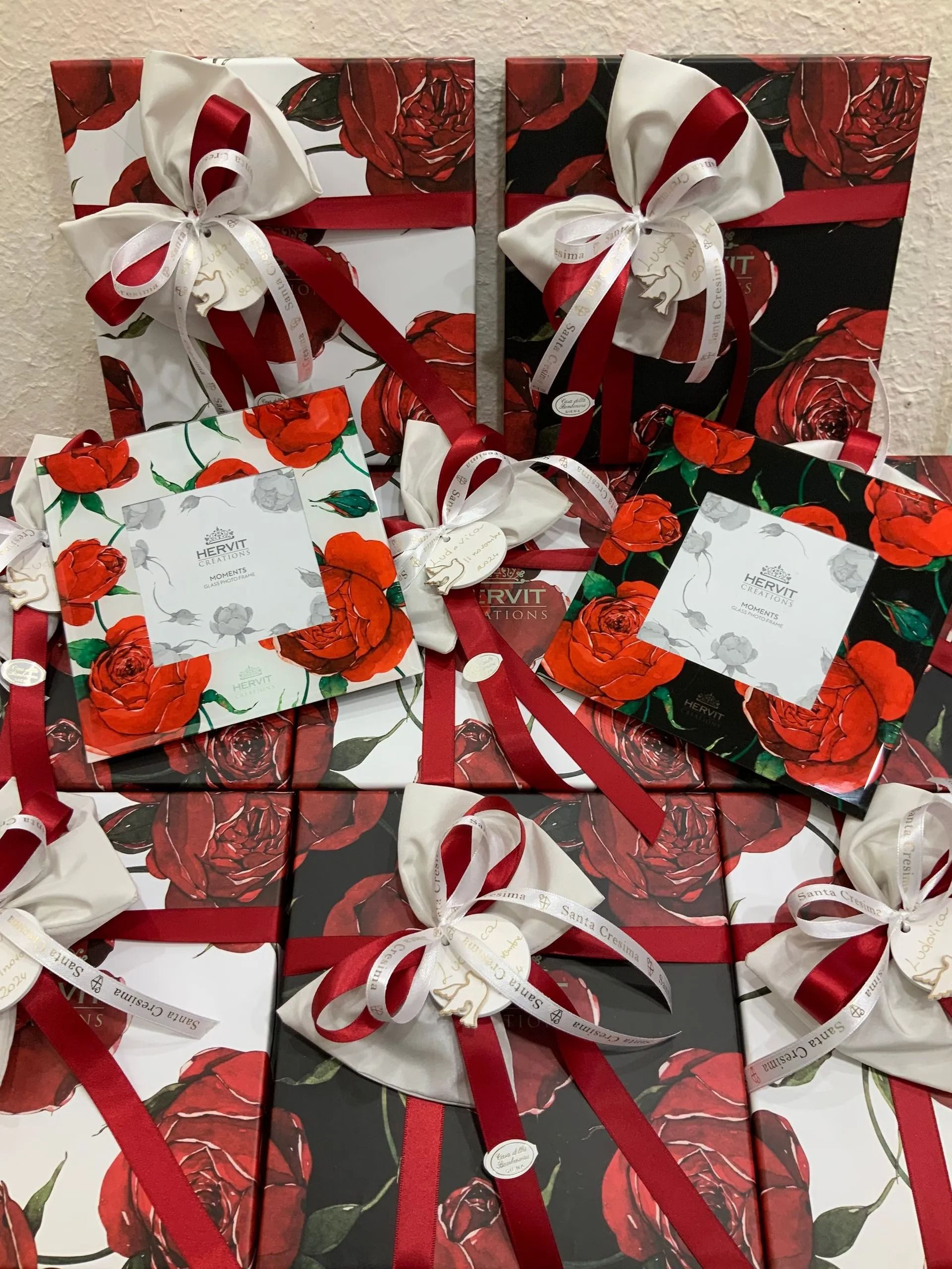 Scatole regalo assortite, rosse e bianche, decorate con fiocchi e motivi natalizi su uno sfondo rosso festivo.