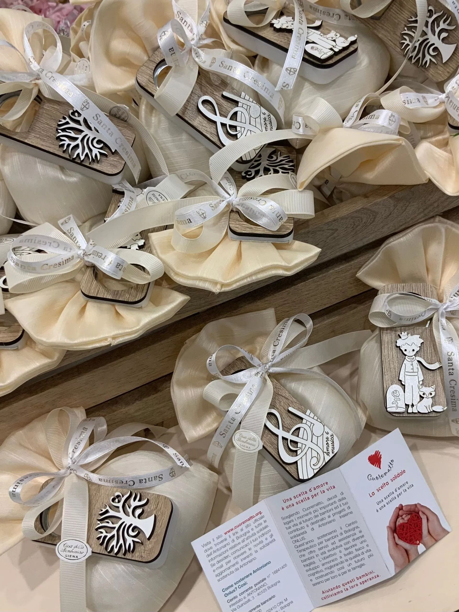 Bomboniere assortite con nastro color crema, etichette in pizzo e un piccolo biglietto di auguri, disposte su un vassoio.