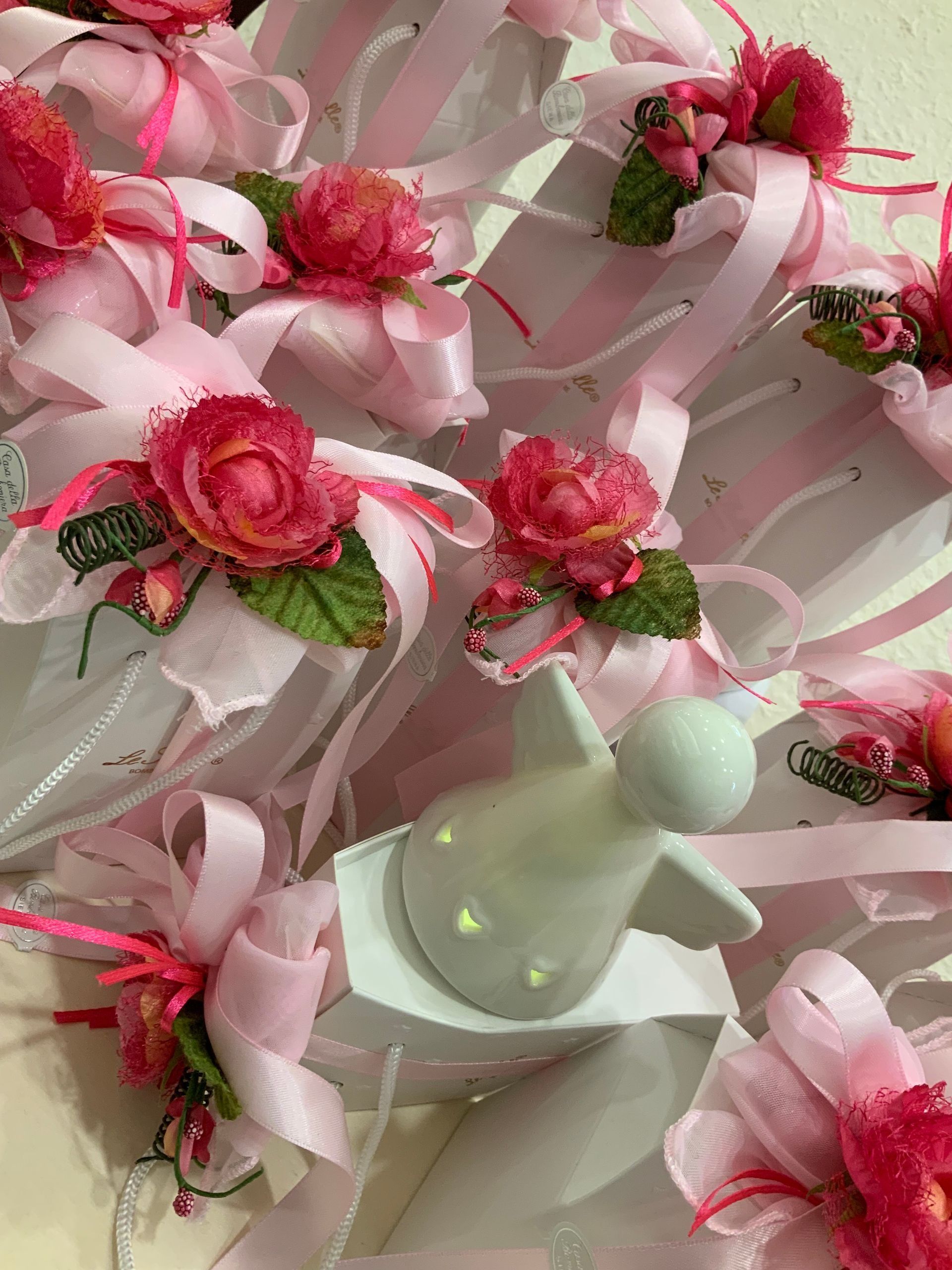 Bomboniere floreali rosa con nastri di raso e una piccola statuetta di uccellino bianco.