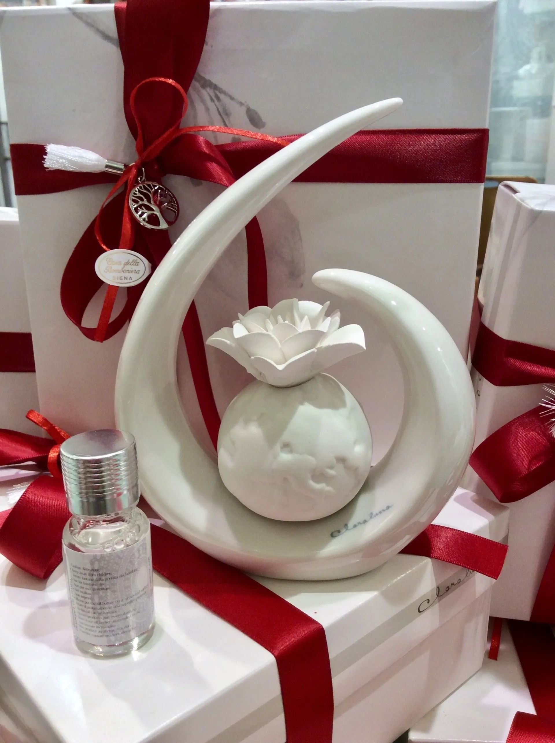 Scatole regalo bianche legate con nastri rossi, con una boccetta di profumo decorativa bianca sul davanti.
