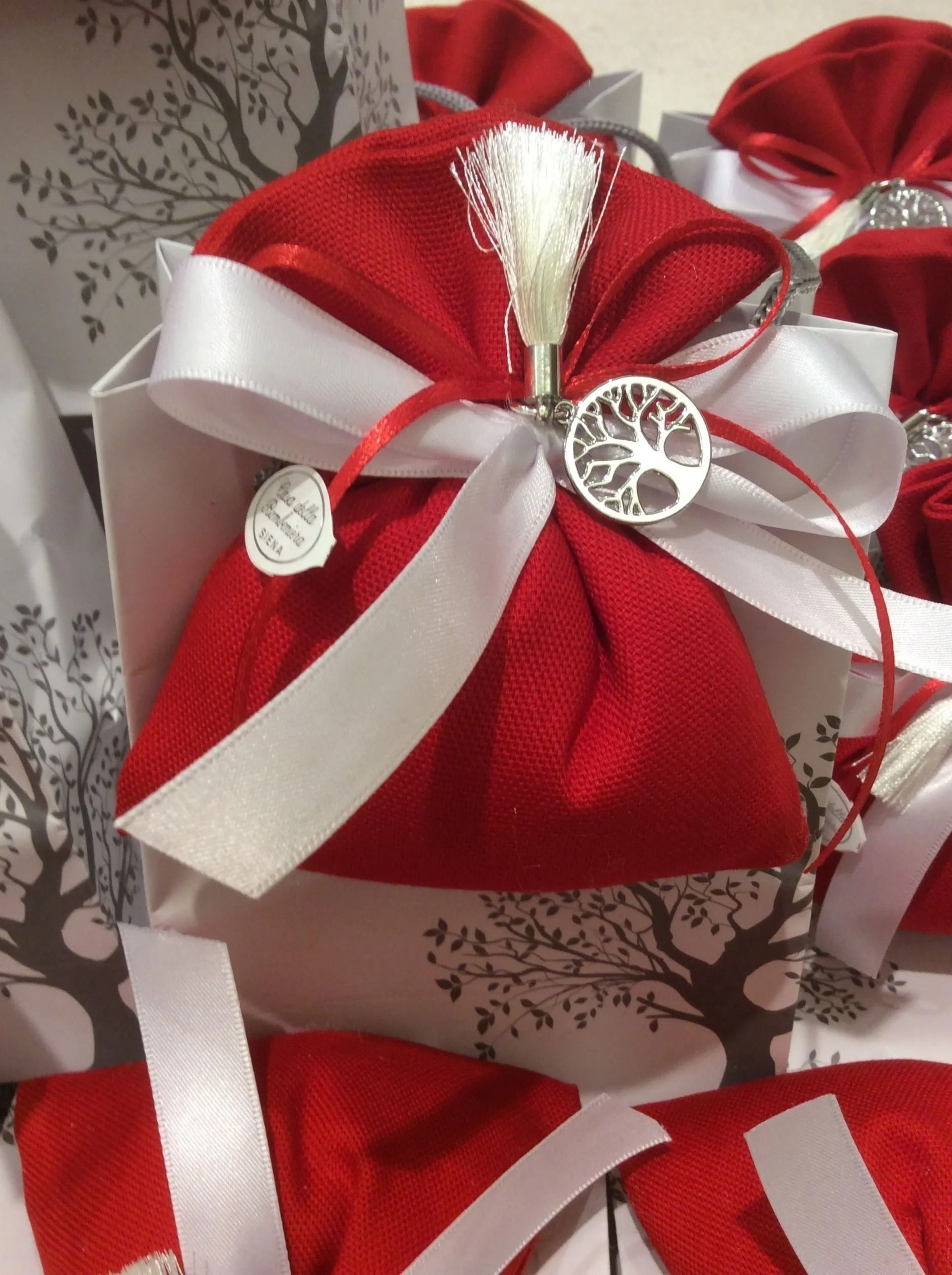 Sacchetti regalo rossi legati con nastri bianchi e decorazioni natalizie argentate su una tovaglia a fantasia.