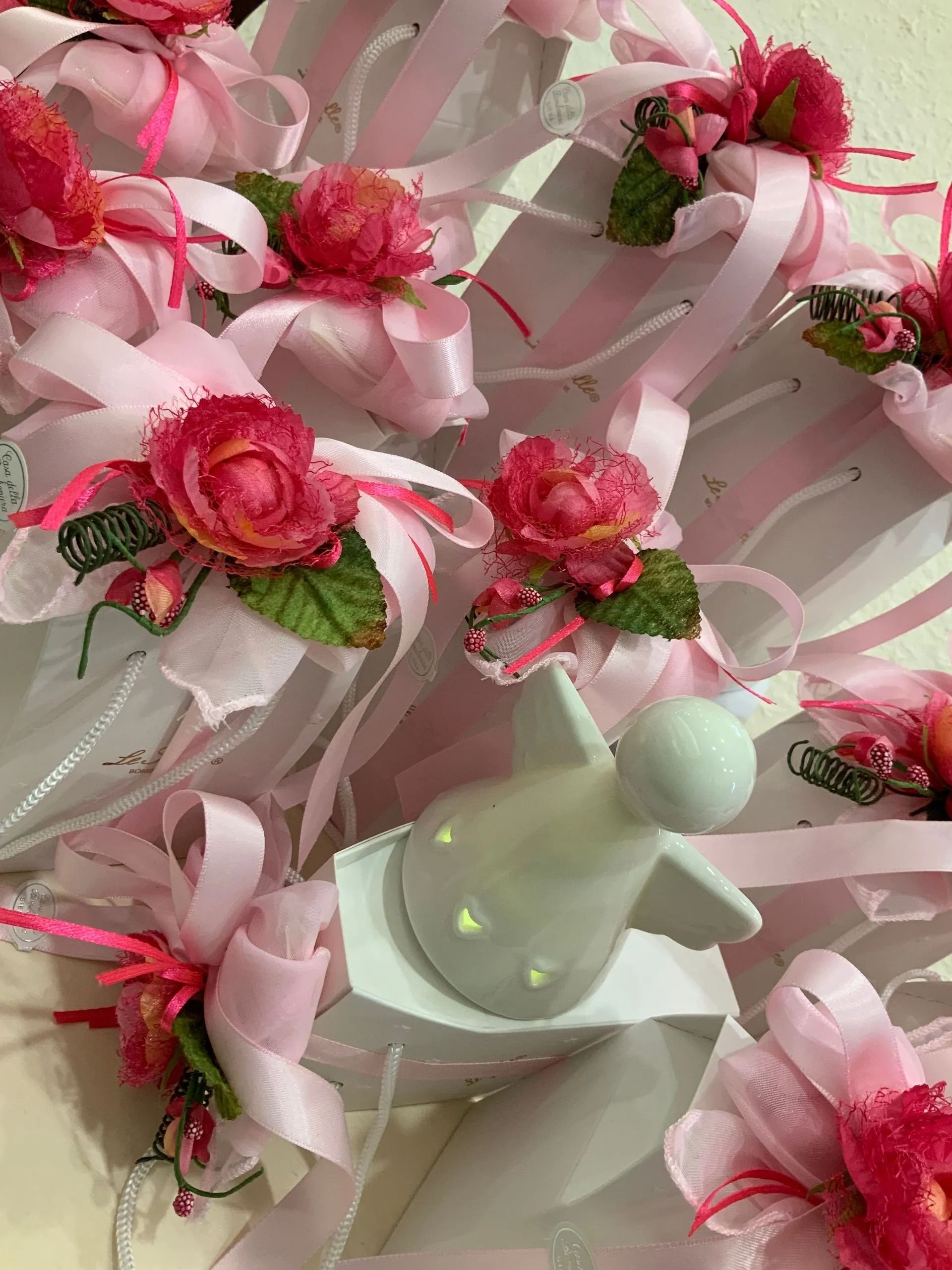 Bomboniere floreali con nastro rosa e rose, accompagnate da un piccolo oggetto bianco e verde menta, disposte su un vassoio.