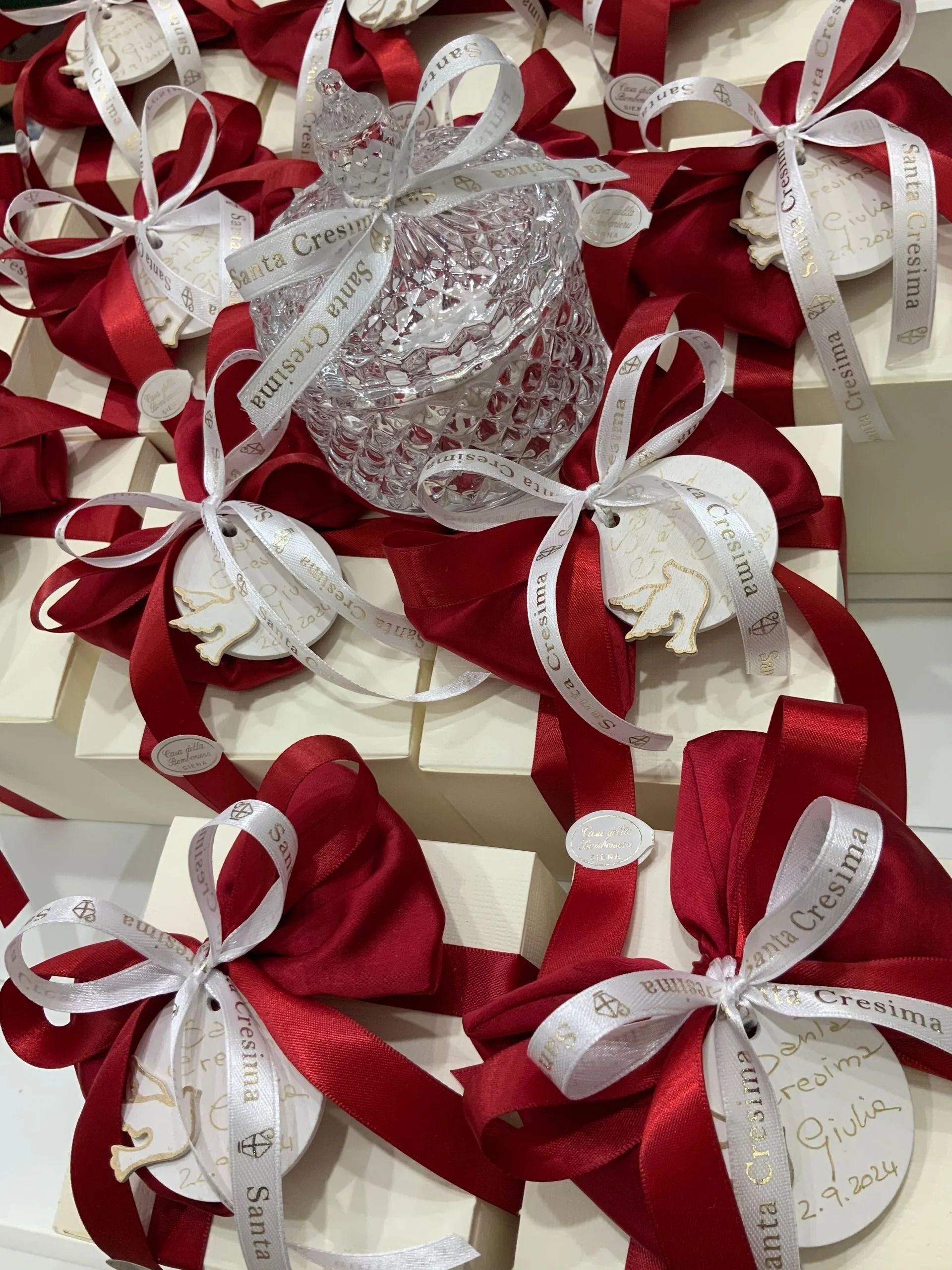Fiocchi di nastro rosso e bianco con centrini di pizzo disposti su un supporto decorativo.