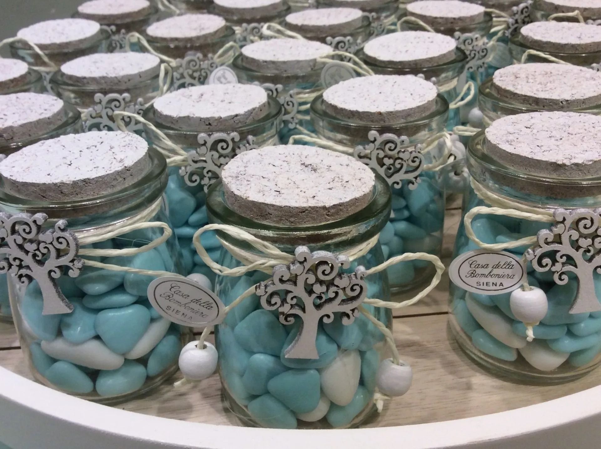 File di barattoli di vetro pieni di caramelle blu e bianche, legati con nastri e cartellini decorativi.
