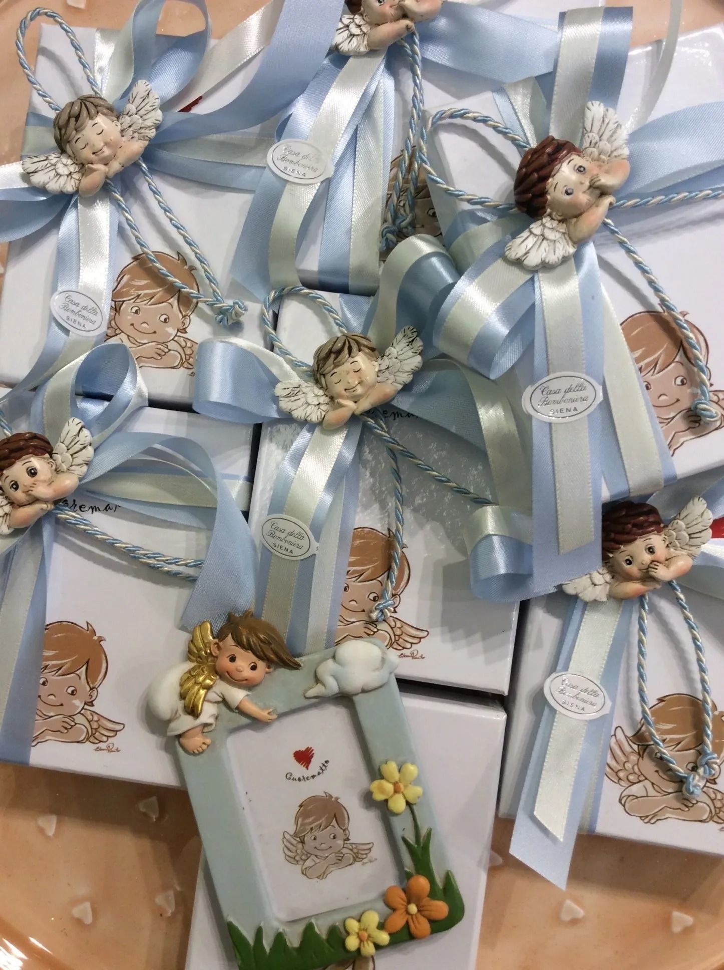 Scatole regalo con nastri blu e decorazioni floreali, sormontate da piccole teste di bambola e ornamenti a forma di angelo.