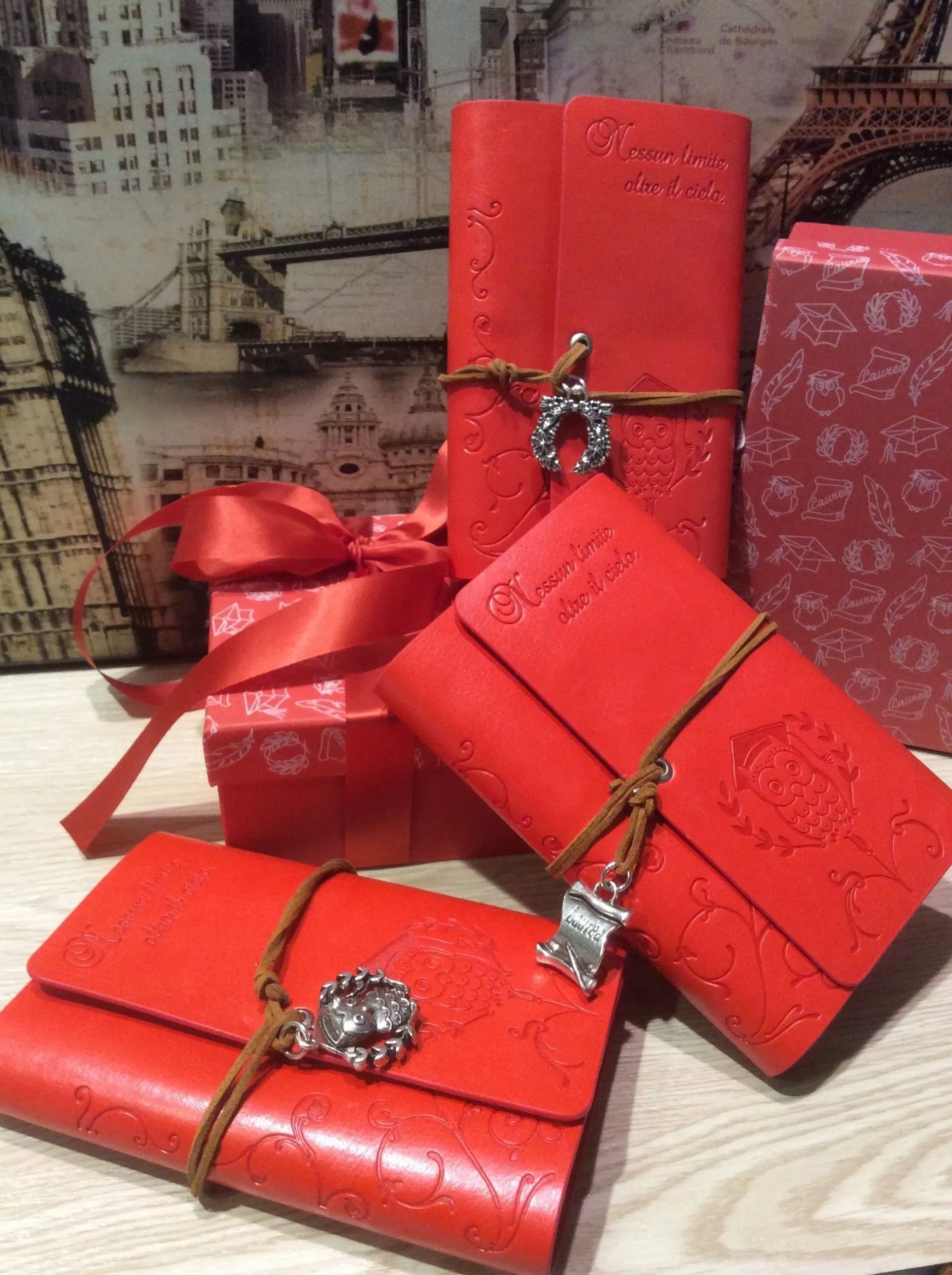 Scatole regalo rosse legate con un nastro dorato, impilate su una superficie di legno chiaro.
