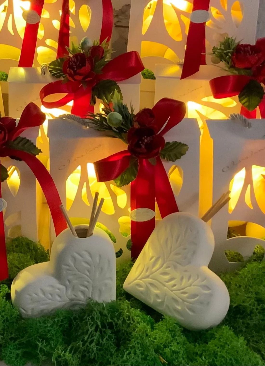 Candele a forma di cuore con nastri rossi e rose su muschio verde, delicatamente illuminate contro uno sfondo caldo e luminoso.