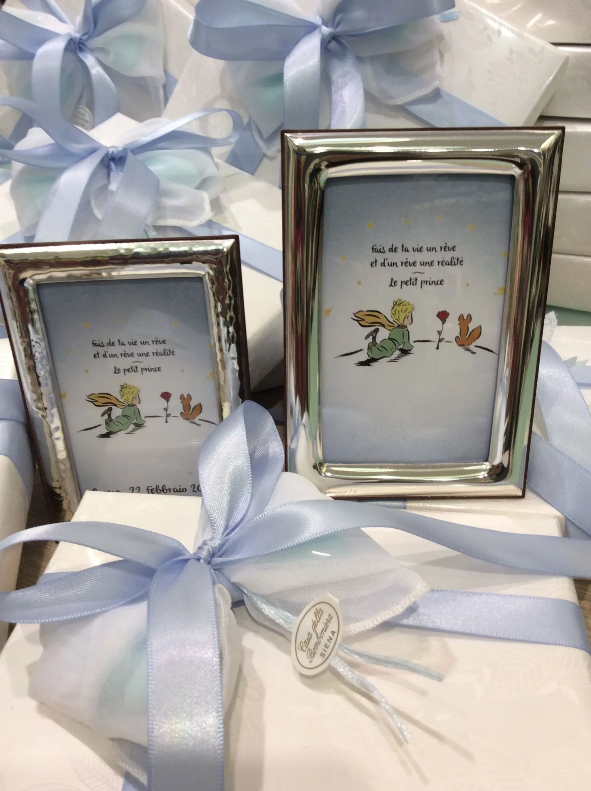 Due cornici argentate su scatole regalo con nastro blu, decorate con fiori bianchi e farfalle.