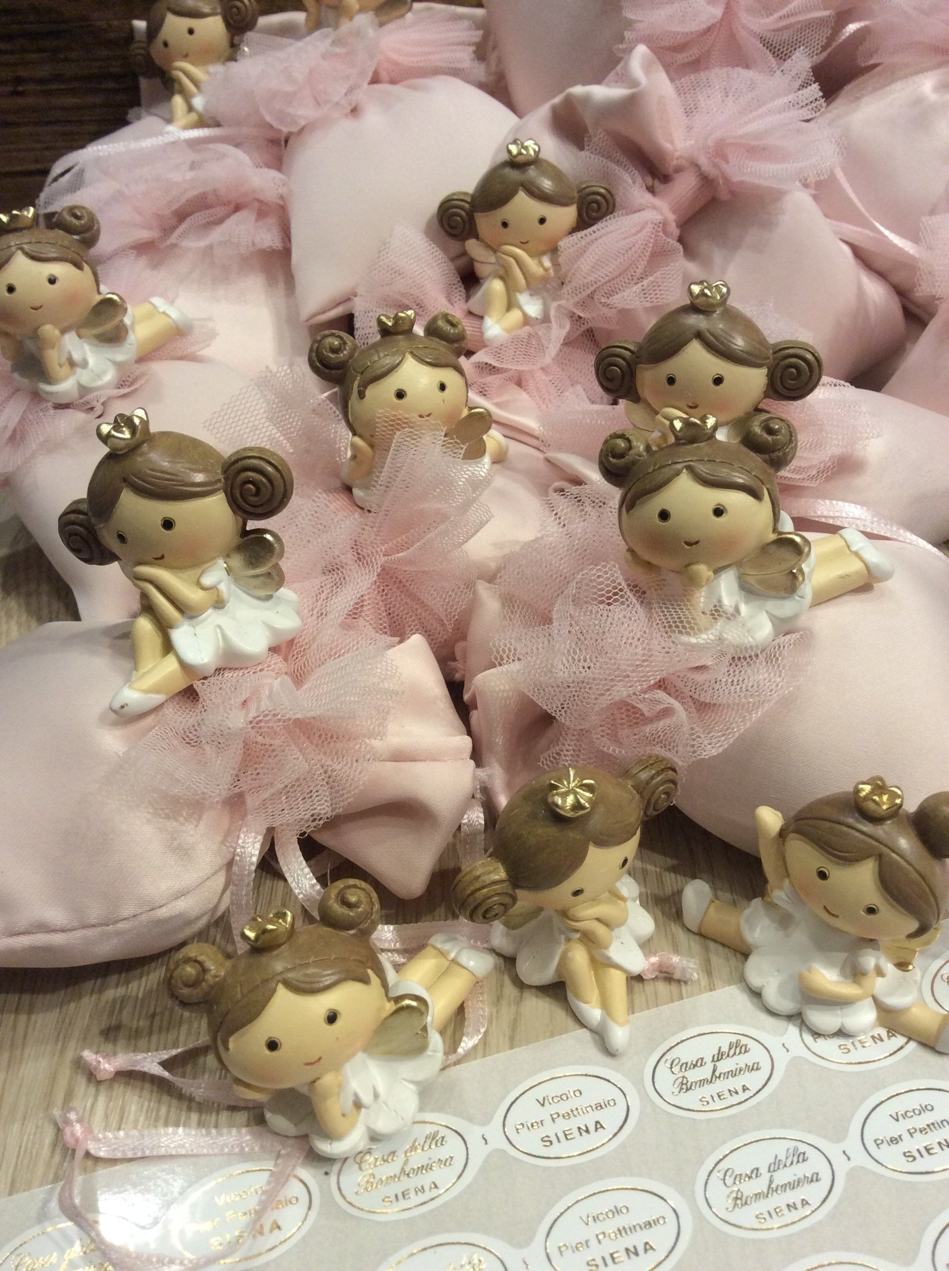 Piccole statuine di angeli adagiate su pizzo rosa, con etichette a forma di cuore disposte sotto.